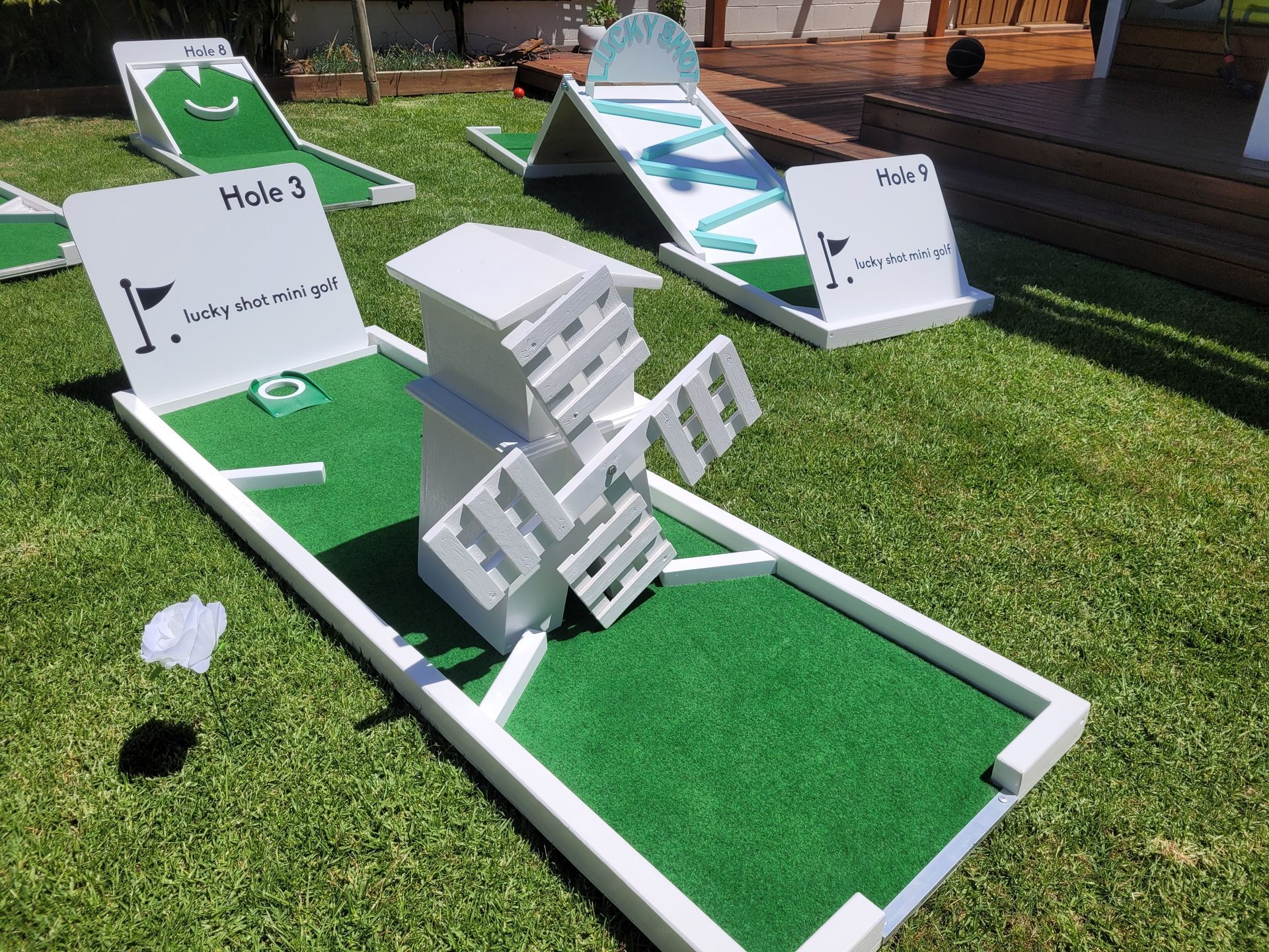 Miniature golf course on grass with white-framed holes and obstacles like a windmill and ramps.