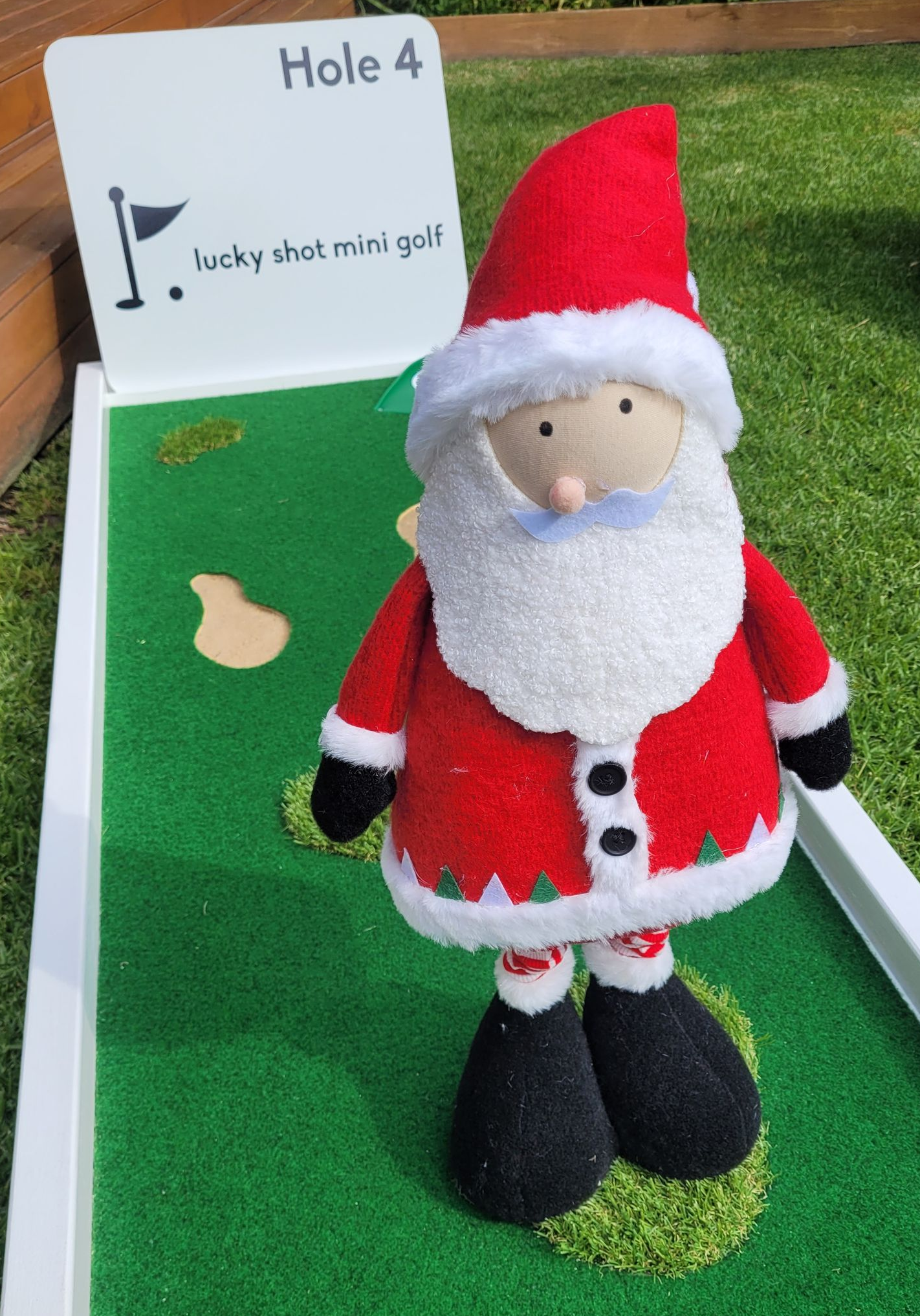 A festive Santa Claus figurine stands on a green mini golf course labeled