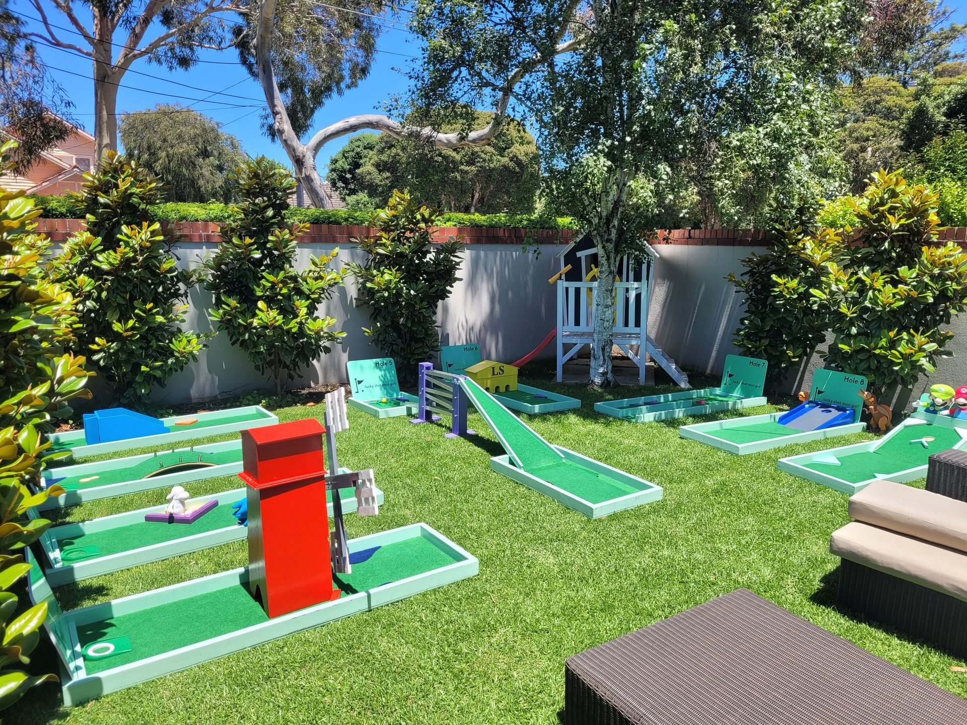 Miniature golf course in a backyard with green turf, various obstacles, and a small playhouse.