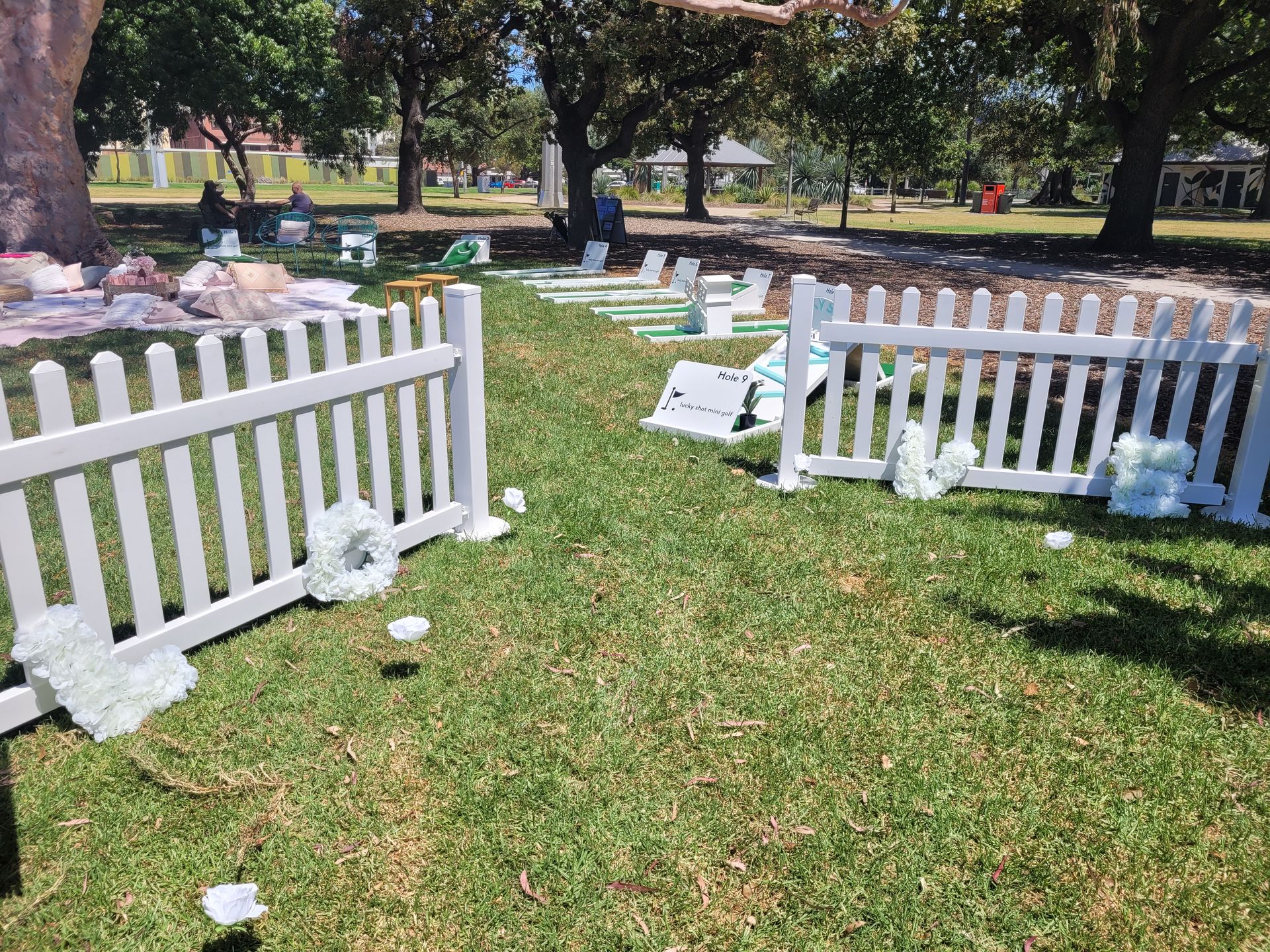 White picket fences with floral decorations on green grass in a park.
