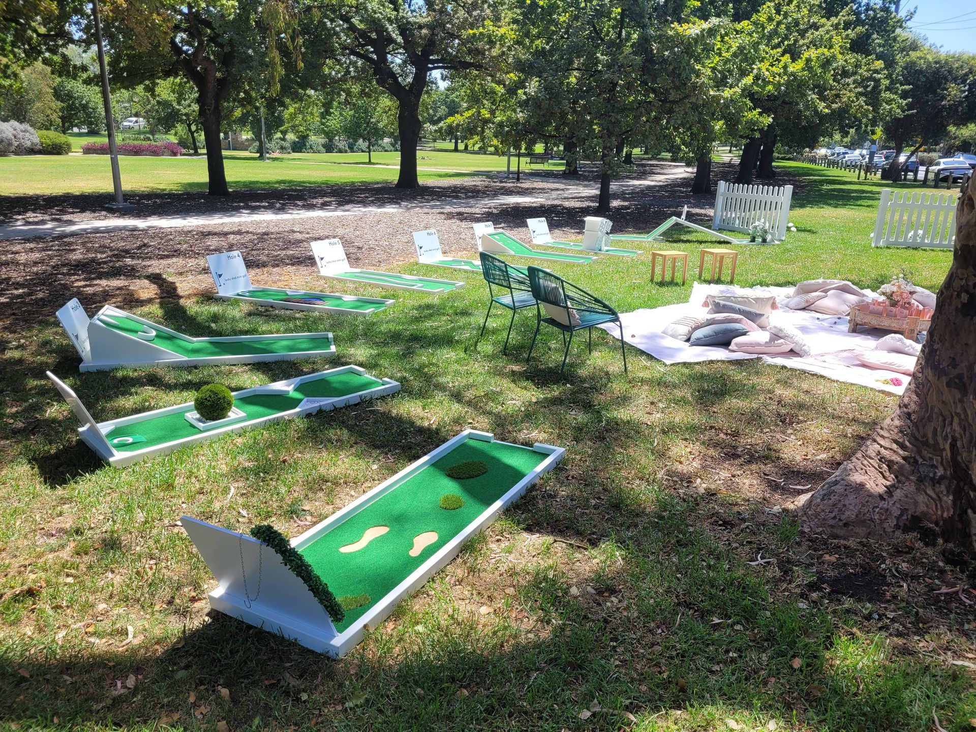 Miniature golf course set up in a park with seating, trees, and fairways.