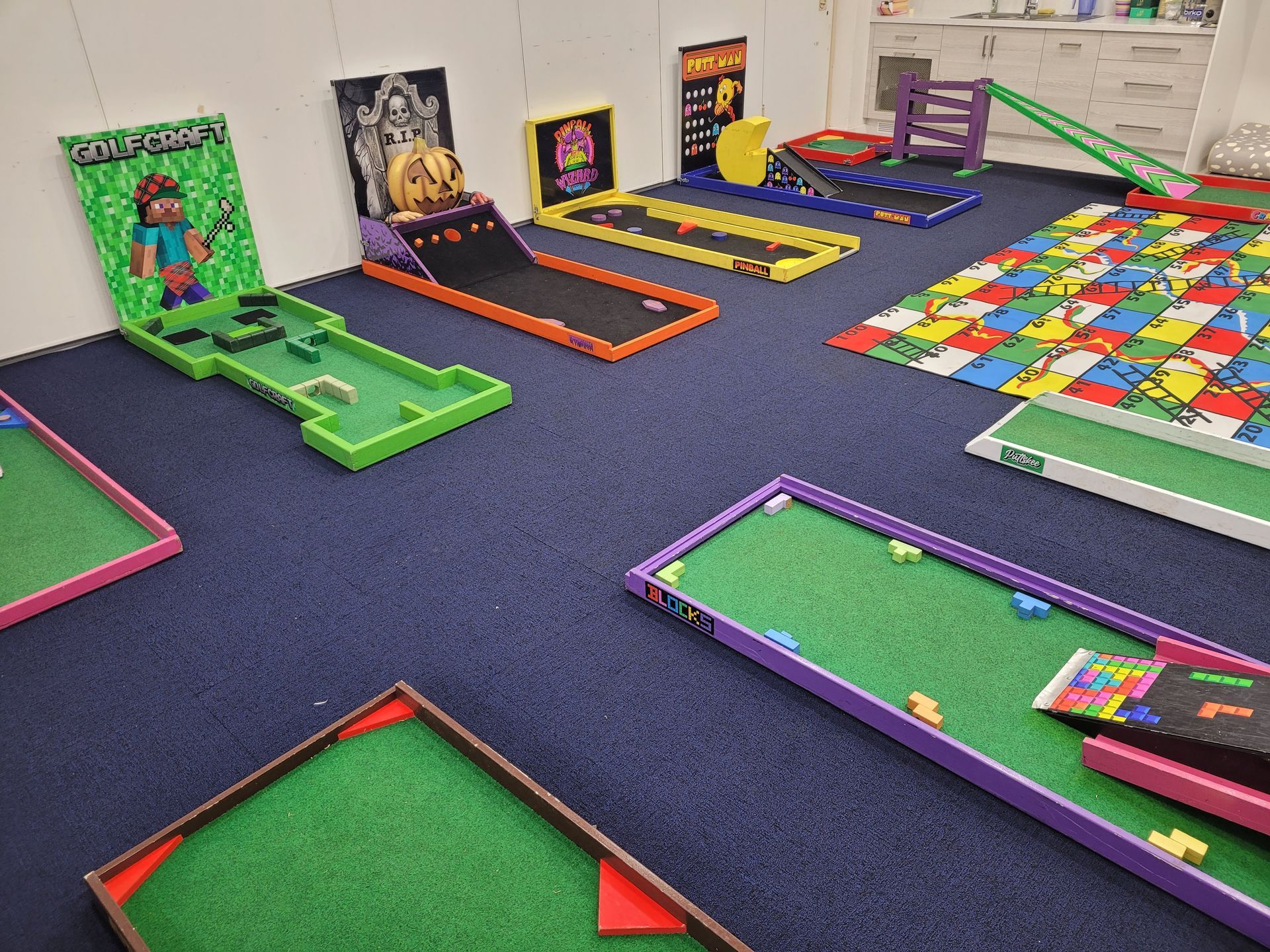 Miniature golf course with various themed holes, including video game themes, on a blue carpet.