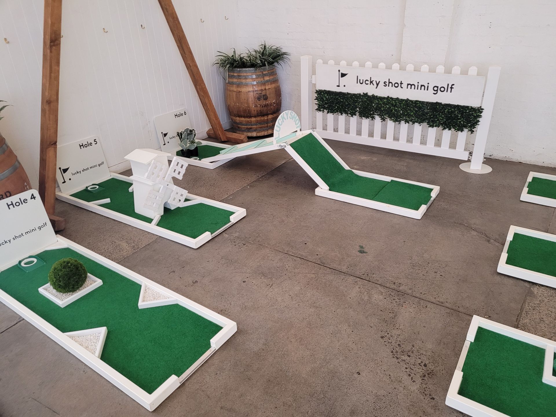 Miniature golf course with white borders, green turf, and obstacles set up indoors.