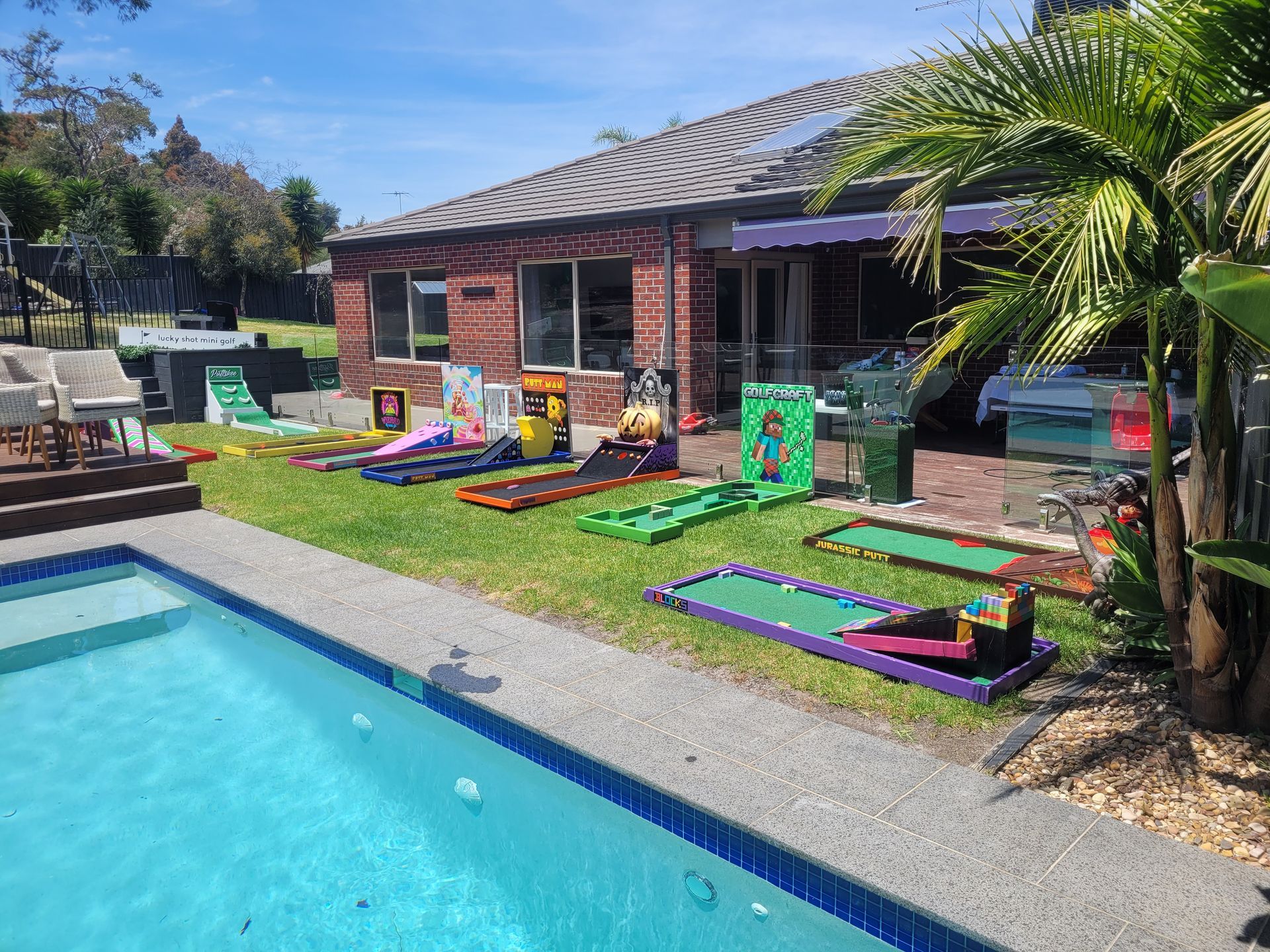 Backyard with mini golf course next to a pool and house; sunny day.