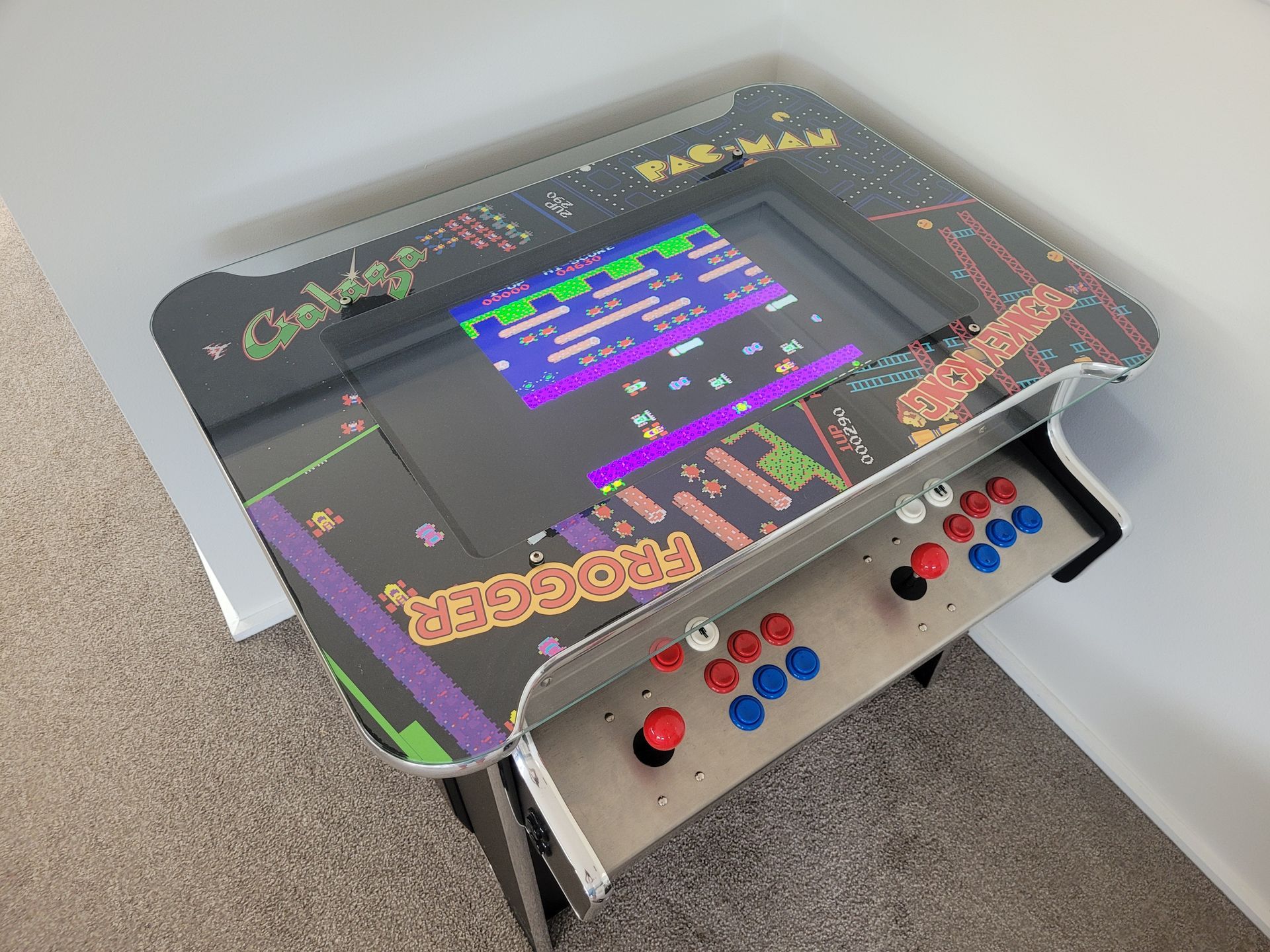 Arcade table with a screen displaying a Frogger game and buttons.