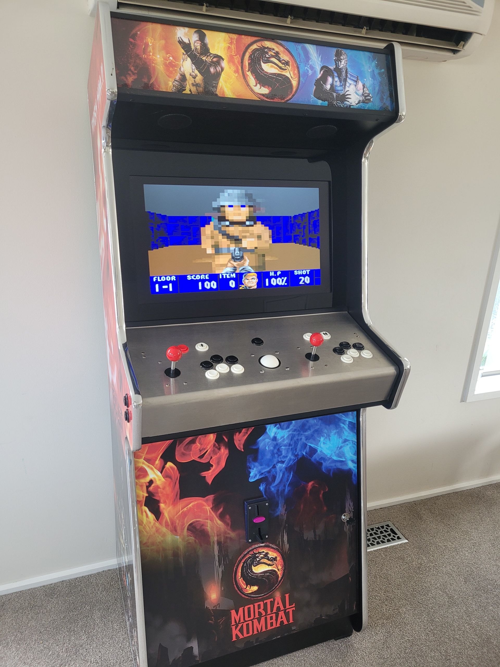 Mortal Kombat arcade cabinet playing a video game.  Gray cabinet with buttons, screen shows a character with a gun.