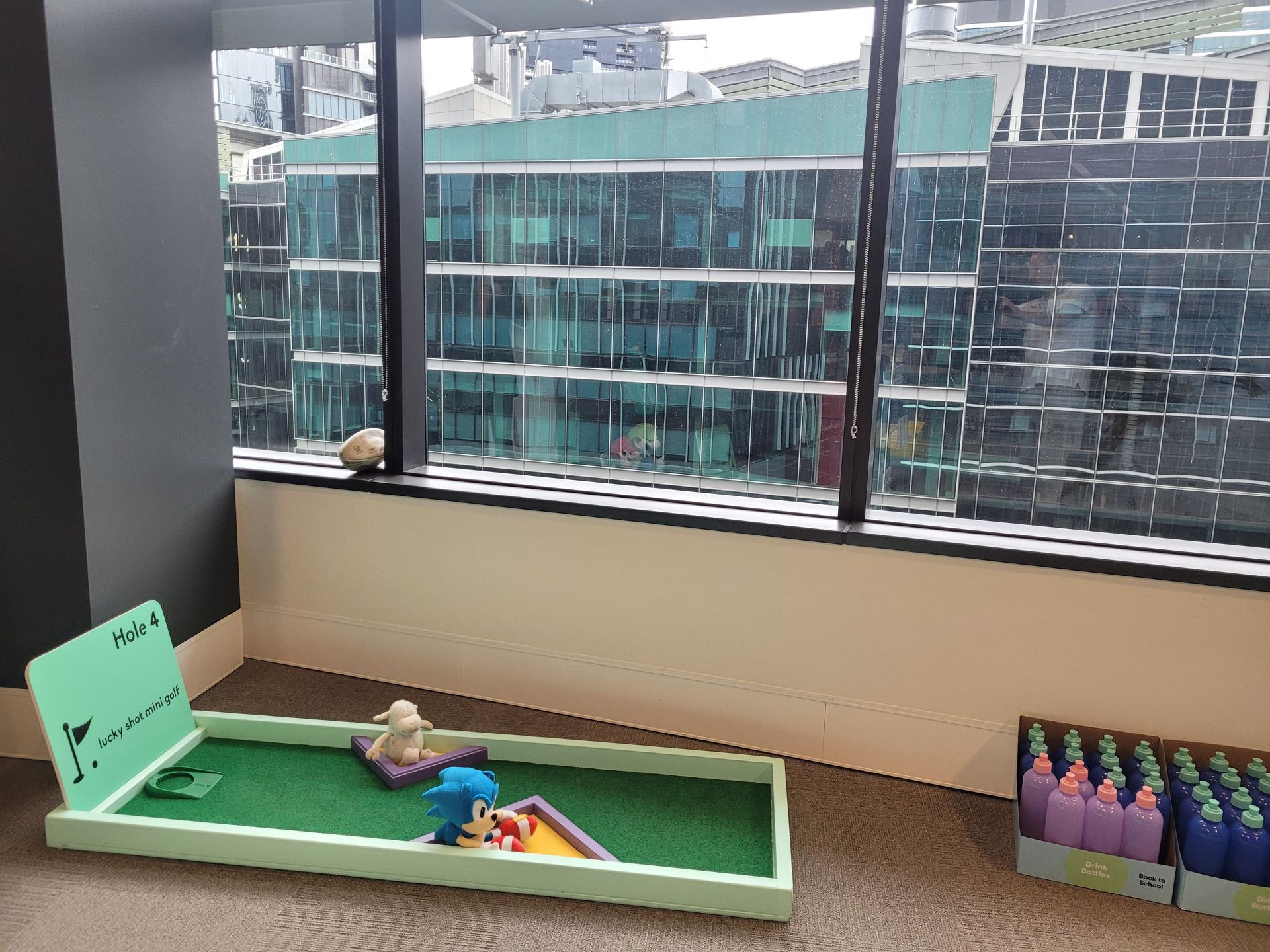 Sunset over an outdoor event with a child playing on a colorful mat. Large building and crowd in background.