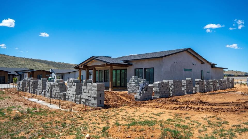 Exterior view of a house under construction with stacked concrete blocks along the perimeter. Sunny day, blue sky.