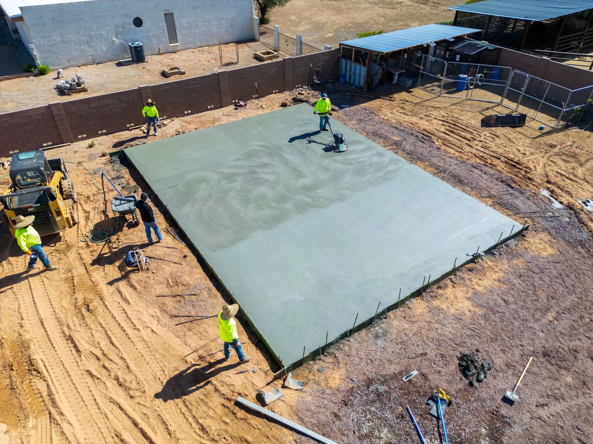 Construction crew smoothing fresh concrete slab on dirt ground outdoors.