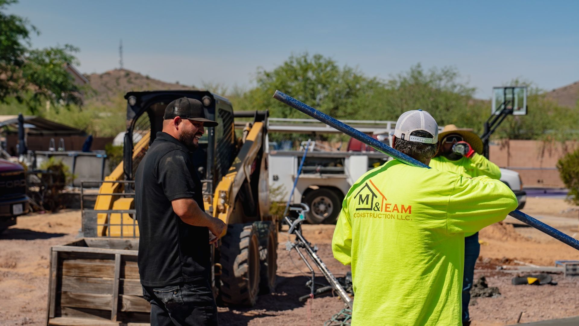 Construction workers with equipment on a sunny day. One carries a long metal pipe.
