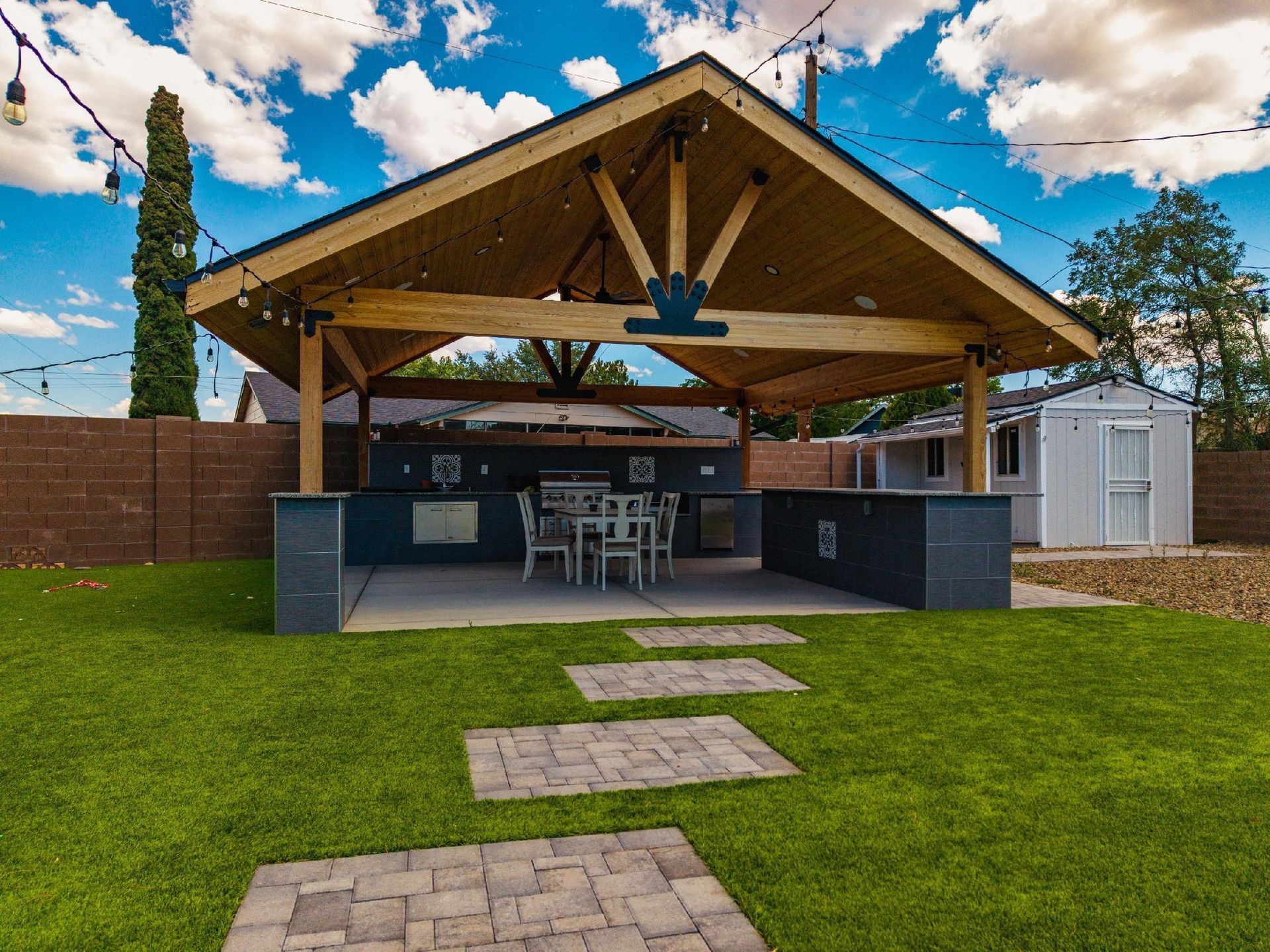 Outdoor kitchen with wooden roof, built-in grill, and dining area on a patio.