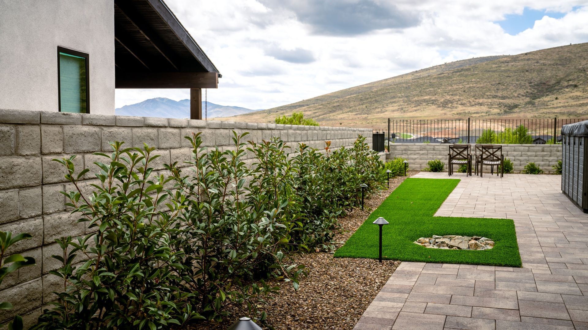Backyard patio with green turf, bushes, stone wall, and mountain view.