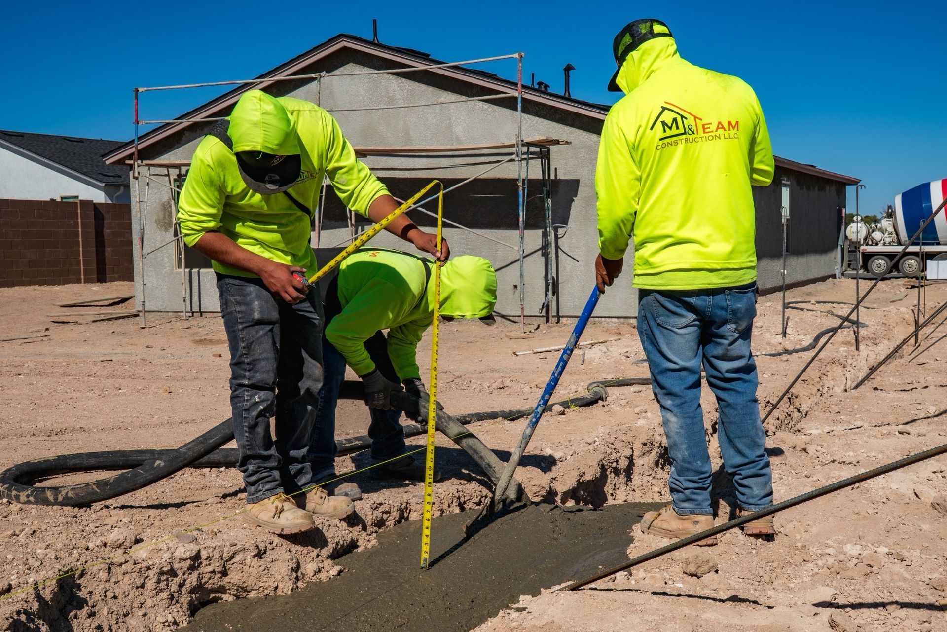 Construction workers pouring concrete into a trench at a building site. They are wearing neon yellow jackets.