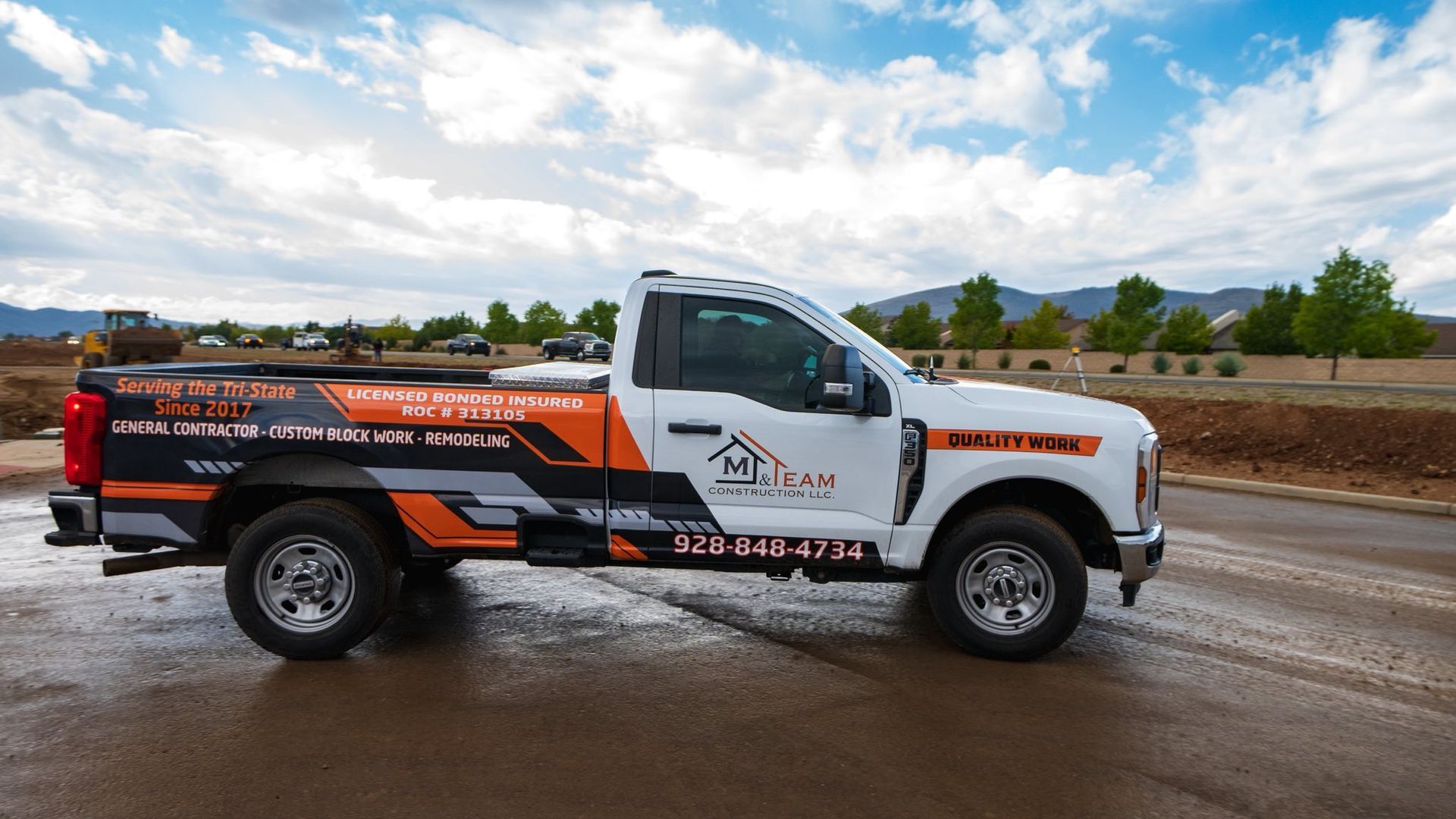 White pickup truck with company logo on the side parked on a road. Cloudy sky, mountains in the background.