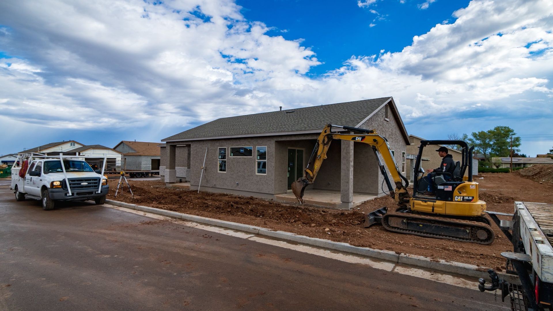 Construction site: Small excavator and work van near a house under construction; overcast sky.