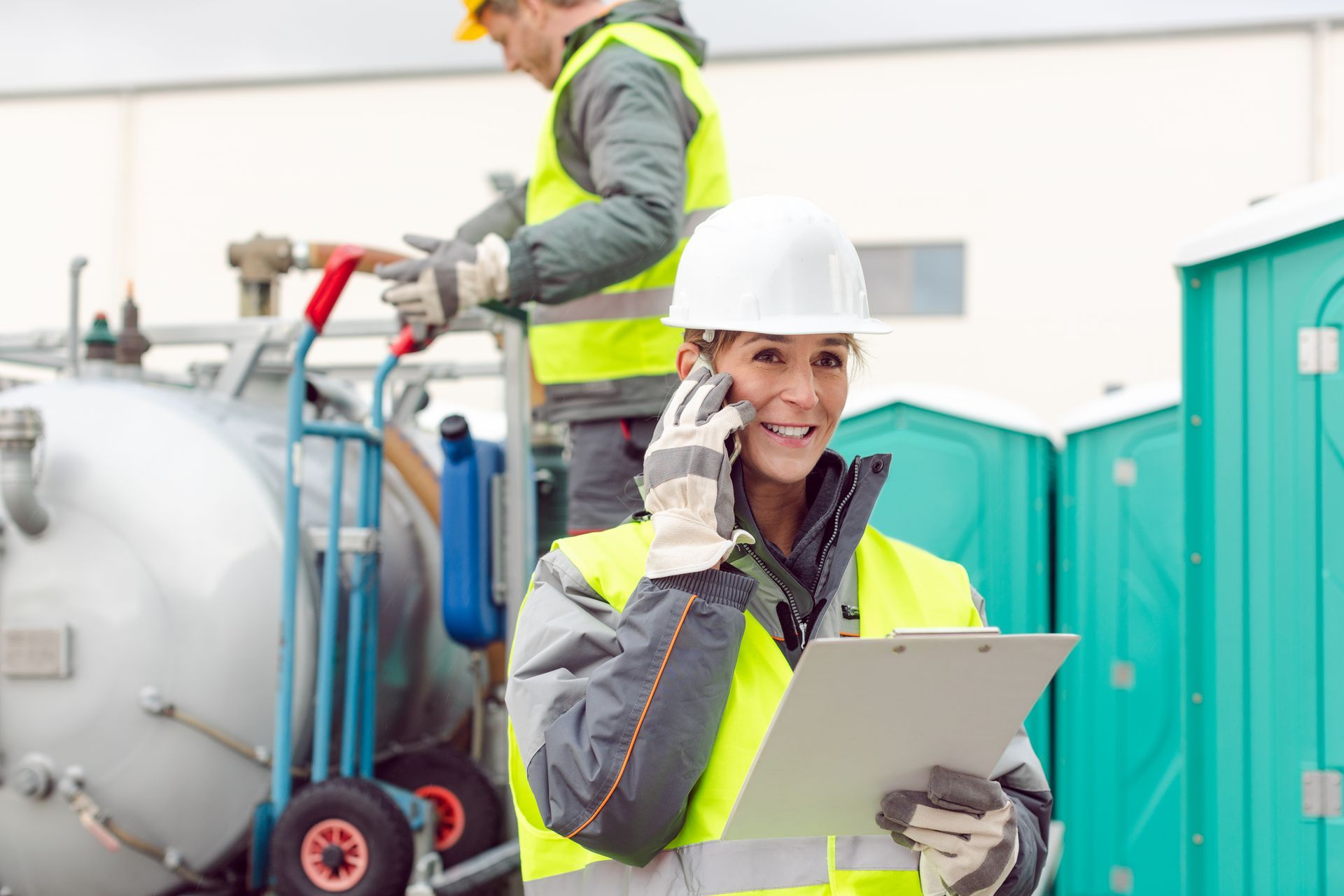 Worker in safety gear using clipboard near portable restrooms and equipment.