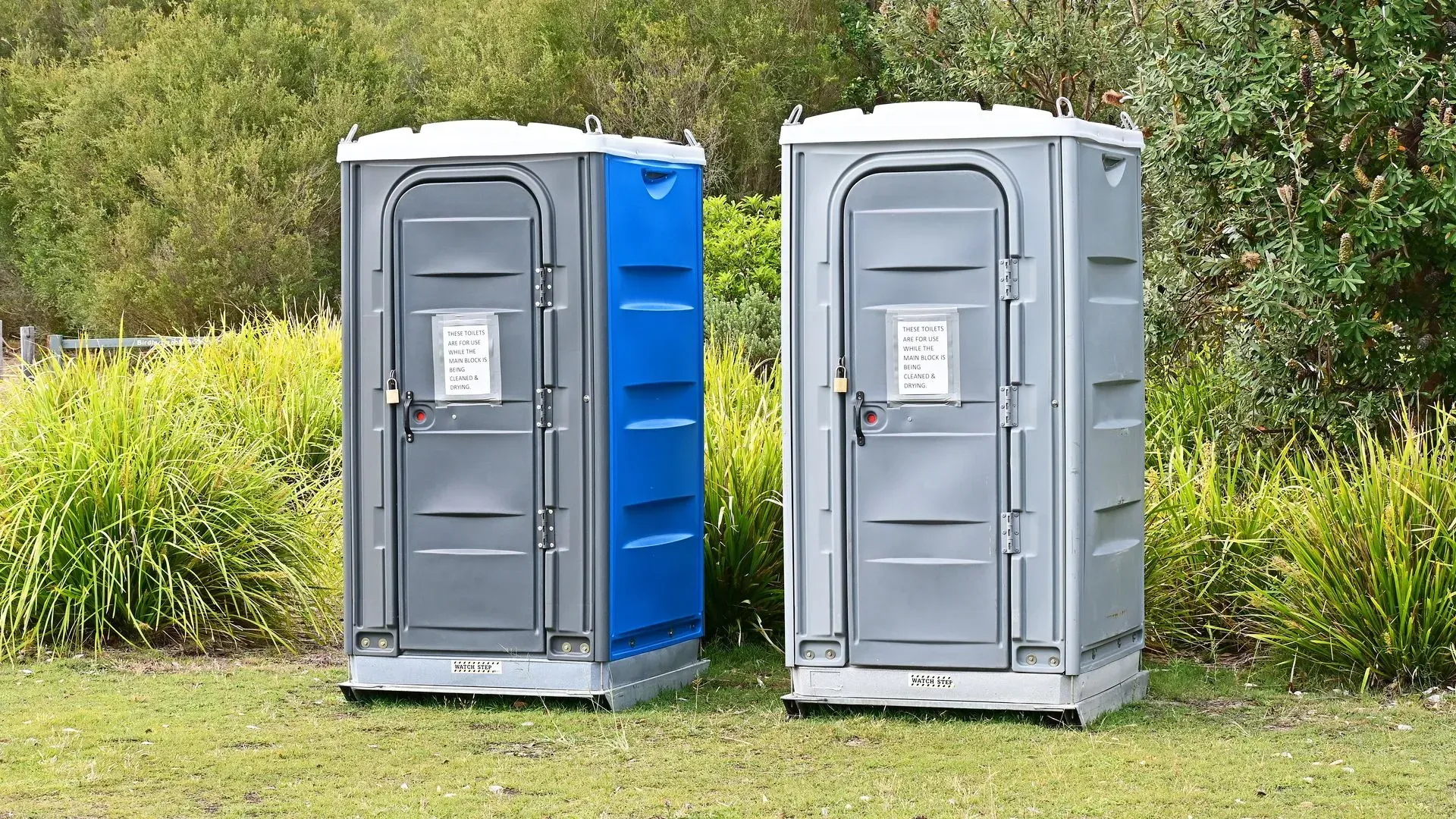 Two portable toilets are sitting next to each other in a grassy field.