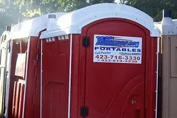A red portable toilet with a phone number on the door.