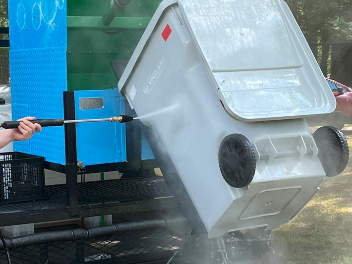 A person is cleaning a trash can with a high pressure washer