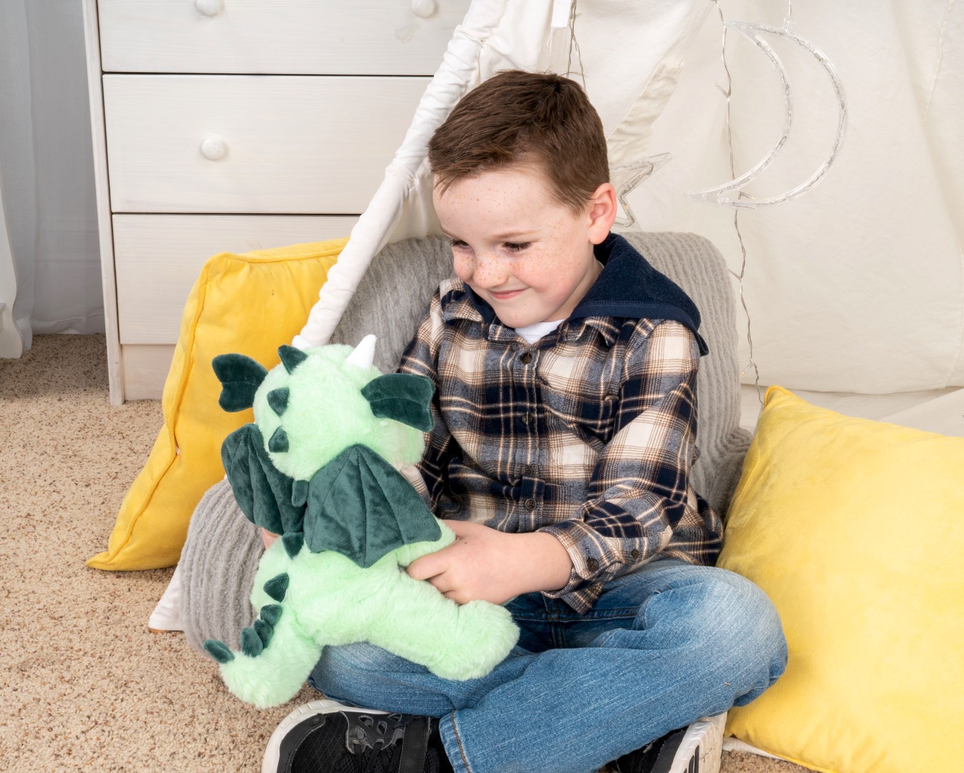A young boy is sitting in a teepee holding a stuffed dragon.