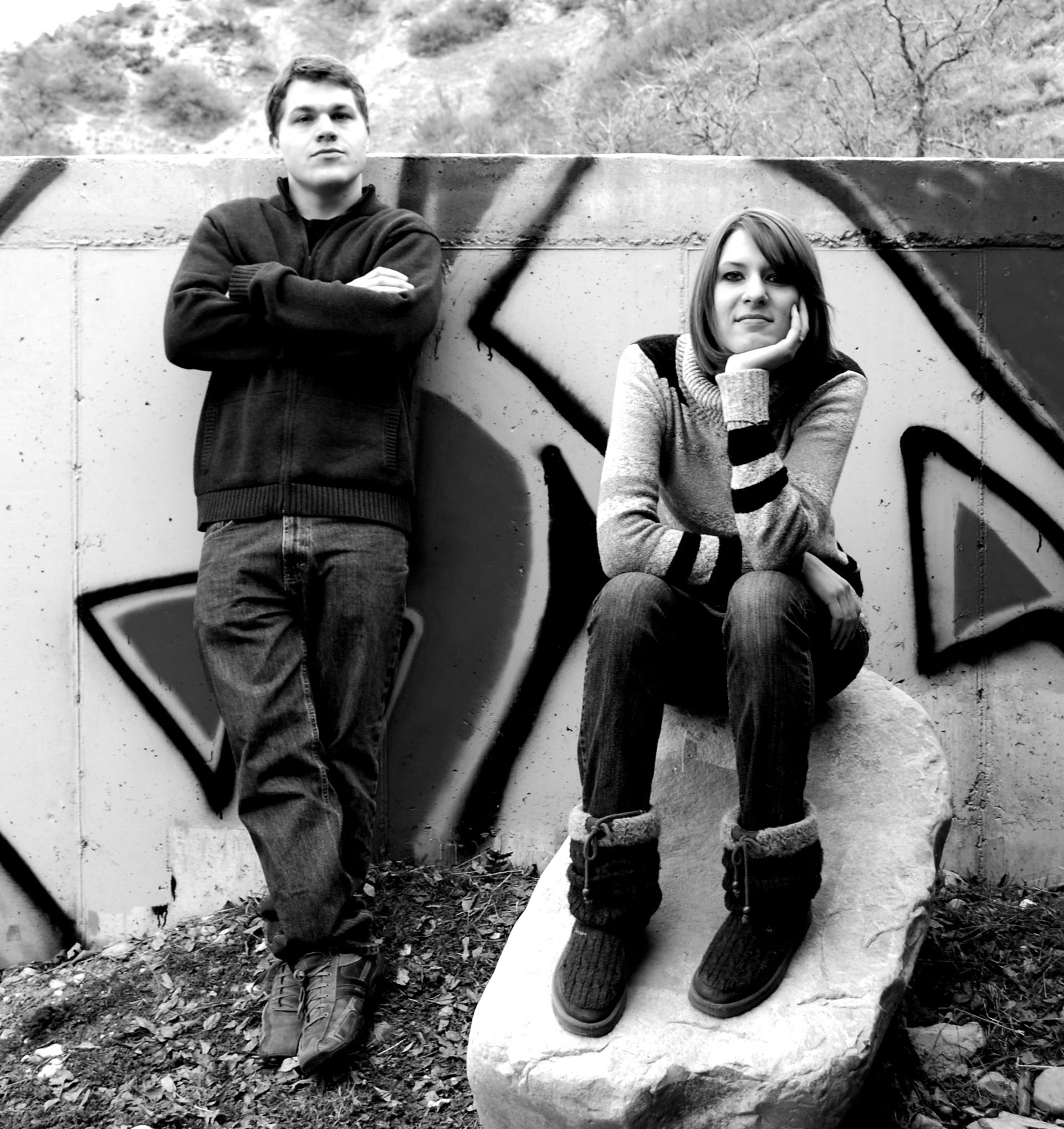 A man and a woman are standing in front of a wall with graffiti on it