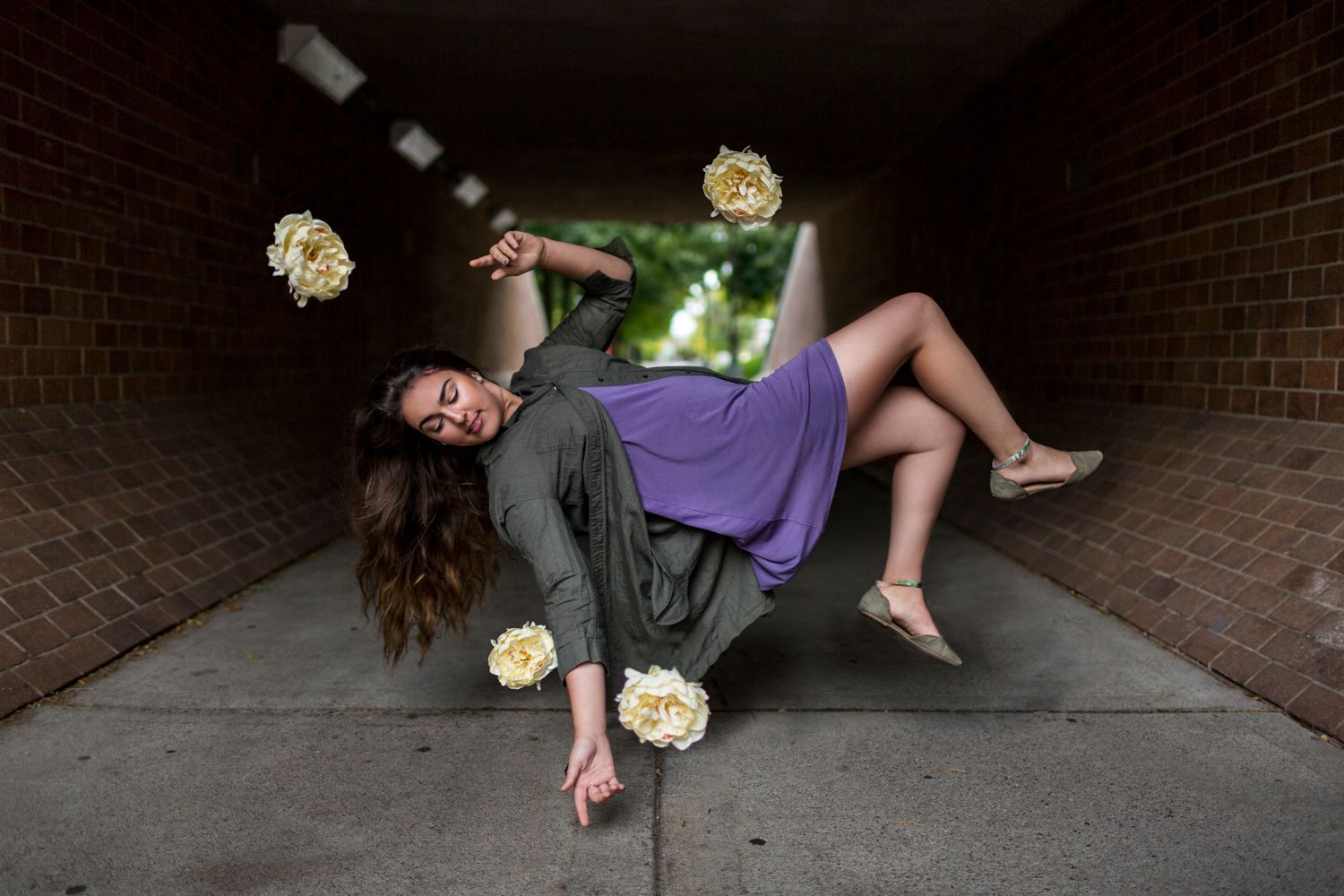 A woman in a purple dress is flying through a tunnel with flowers flying around her.