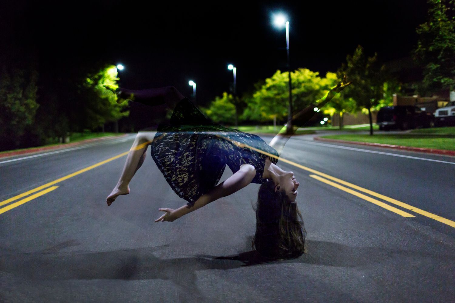 A woman is doing a handstand on the side of a road at night.