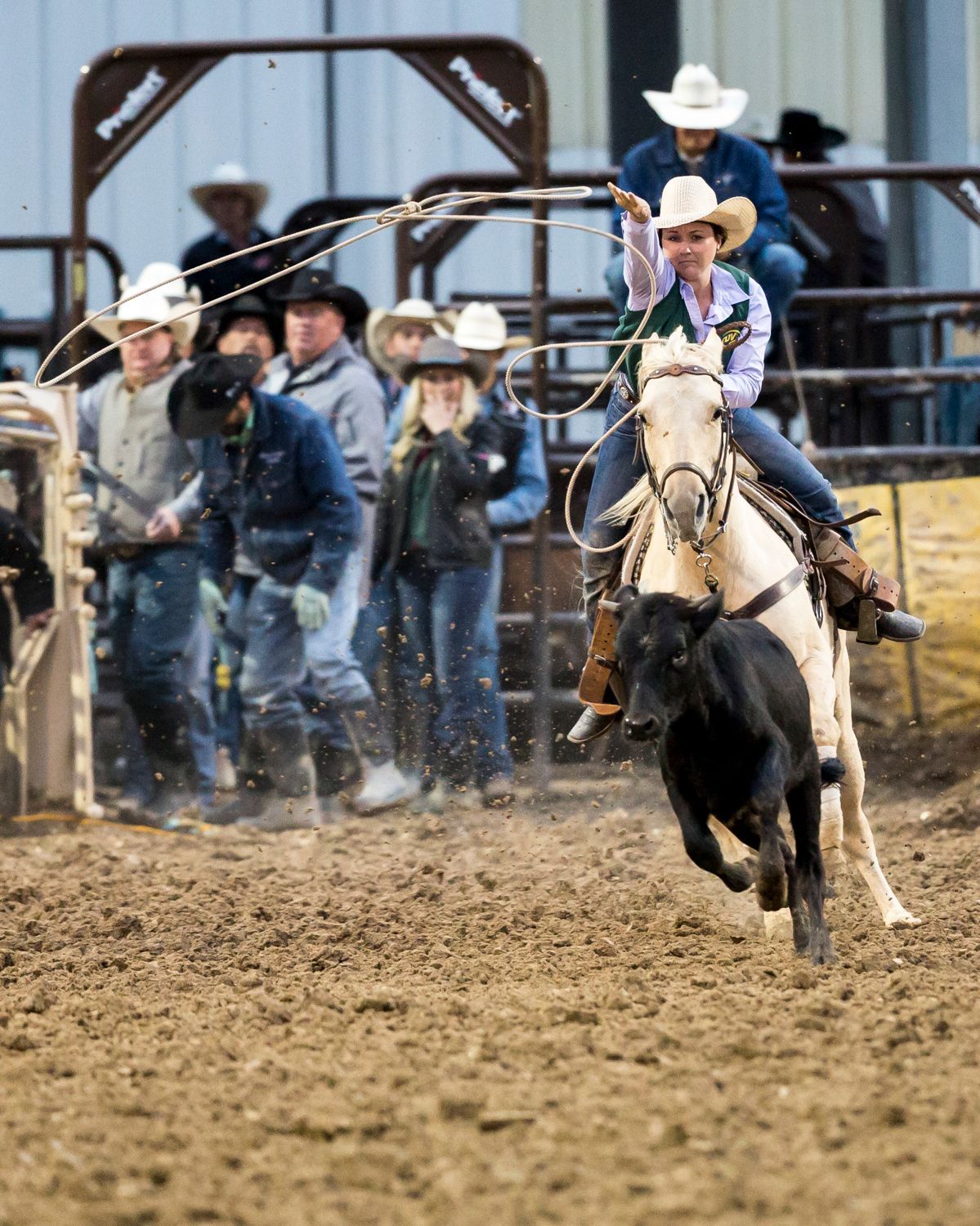A woman is riding a horse in a rodeo while a group of people watch.