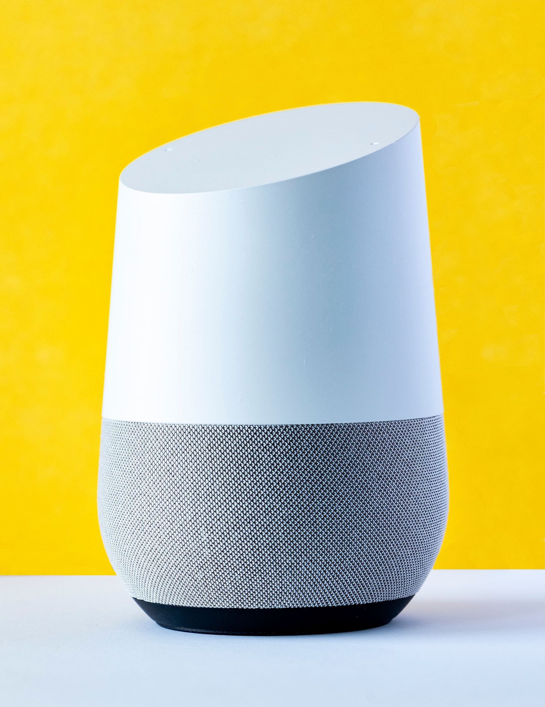 A smart speaker is sitting on a table in front of a yellow background.
