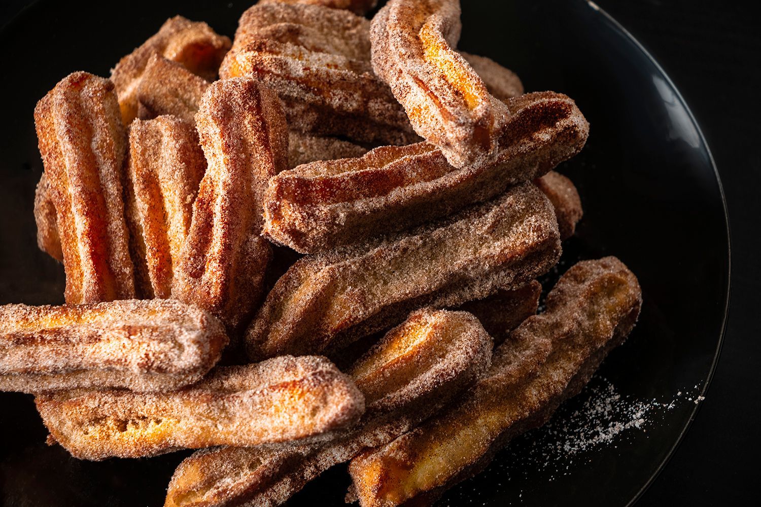 A black plate topped with fried bananas covered in sugar.