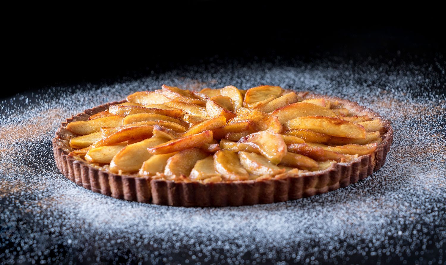 An apple pie covered in powdered sugar on a table.