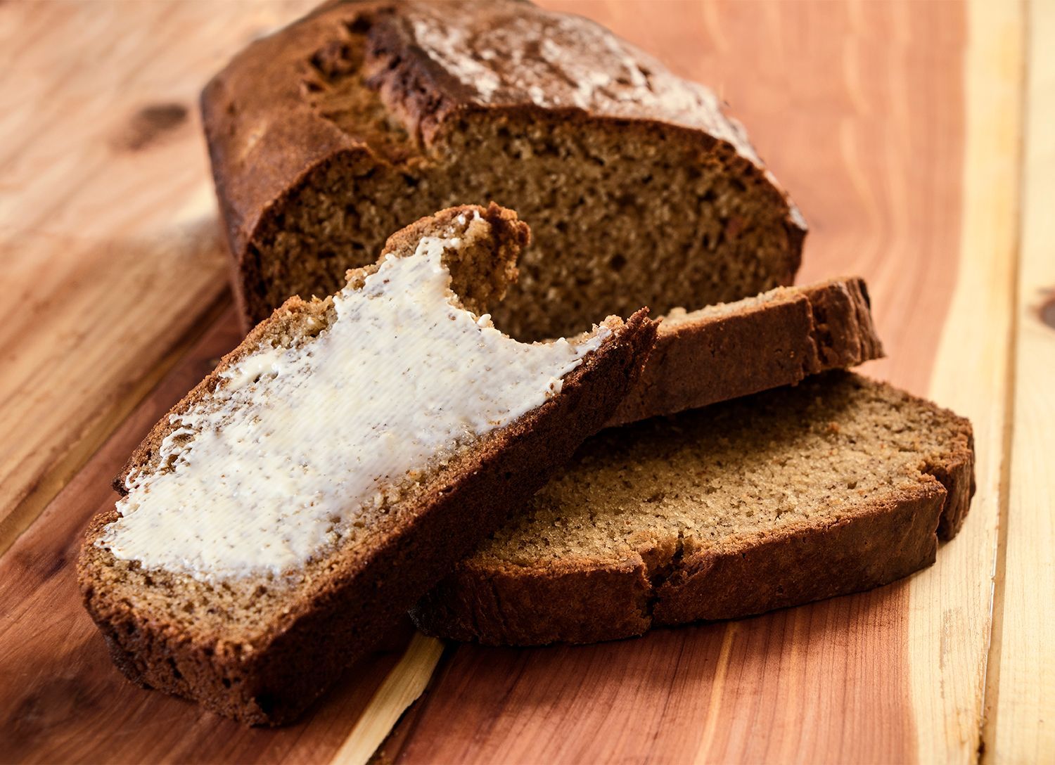 A loaf of bread with butter on it is on a wooden cutting board.