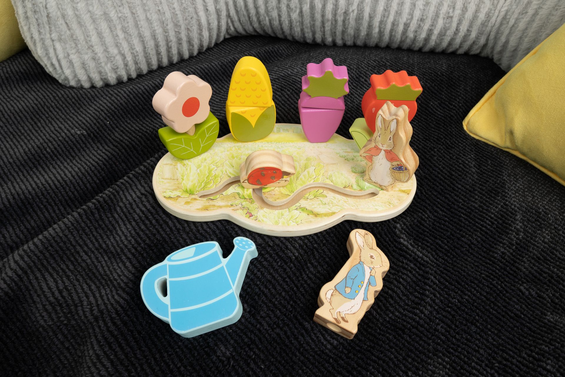 A wooden puzzle with flowers , a watering can , and a rabbit is sitting on a couch.
