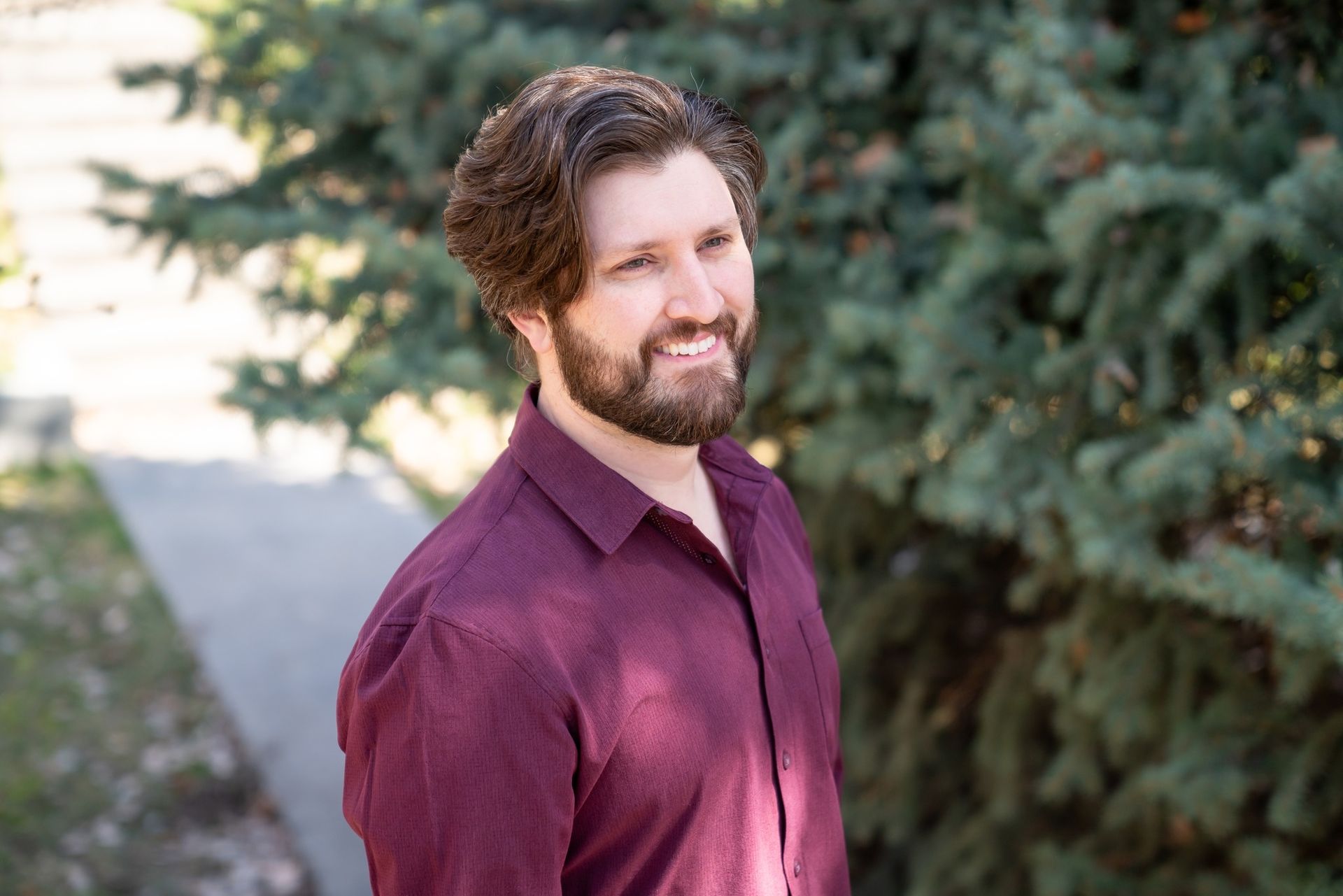 A man with a beard is standing in front of a tree.