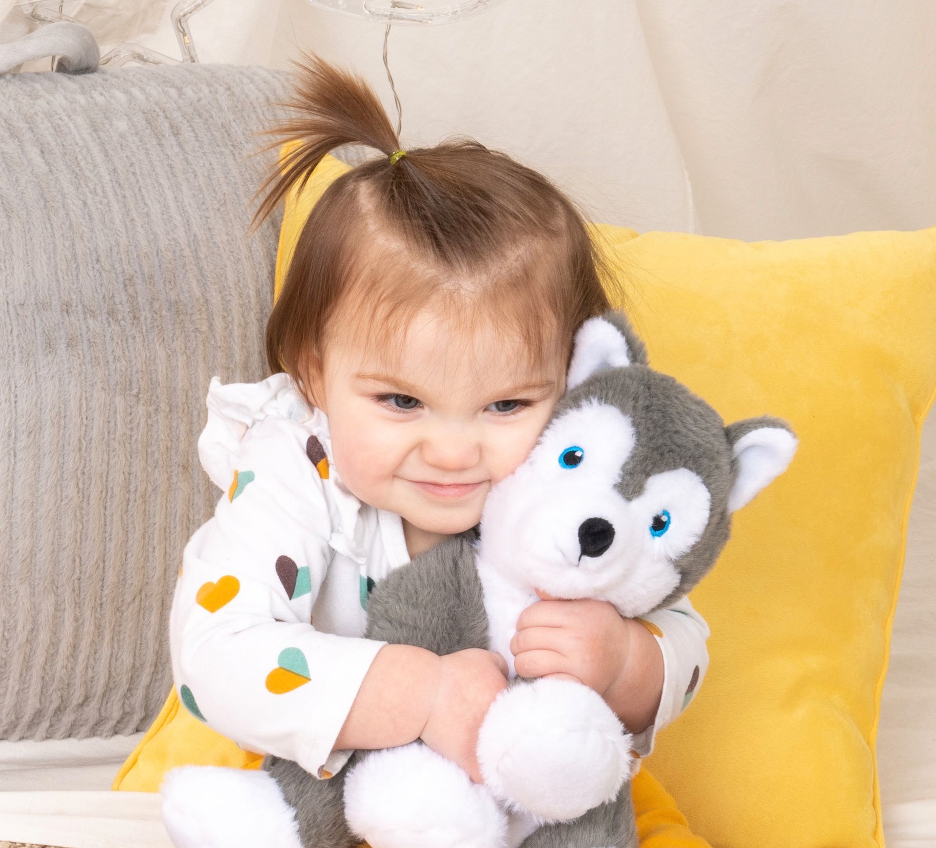 A baby girl is holding a stuffed husky dog