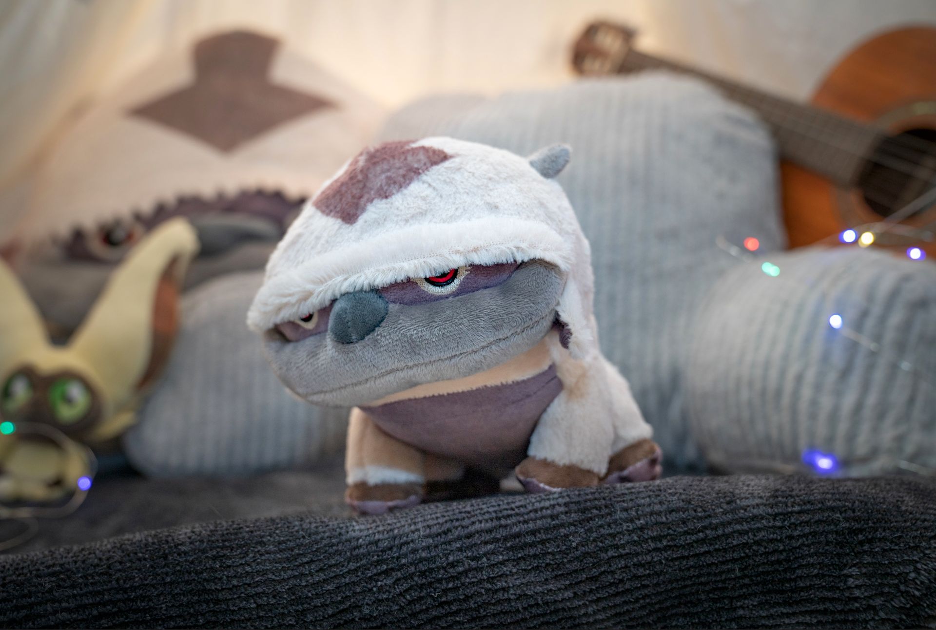 A stuffed animal is sitting on a couch next to a guitar.