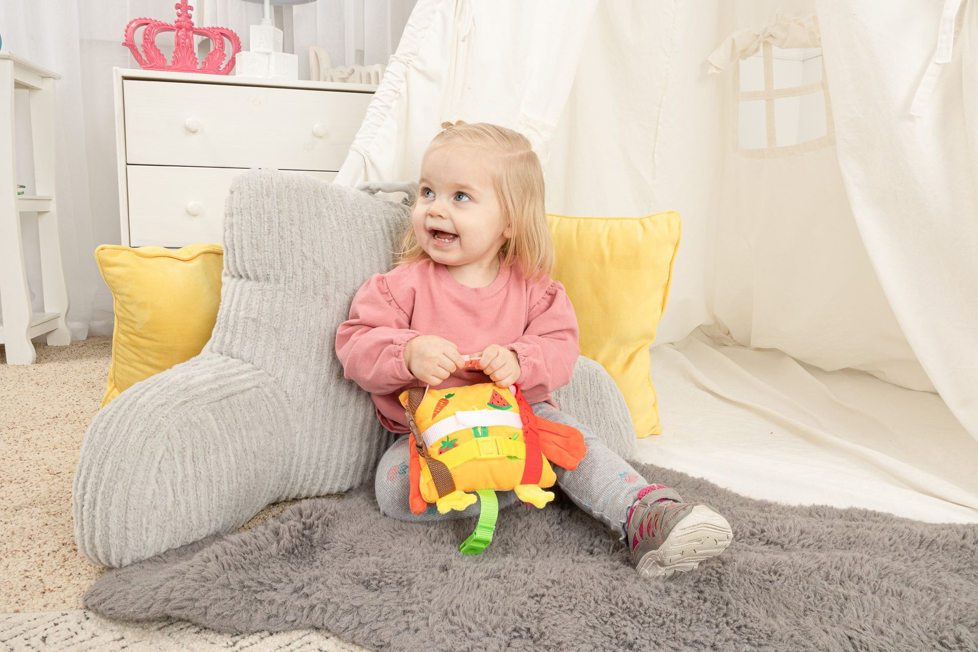 A little girl is sitting in a chair playing with a stuffed animal.