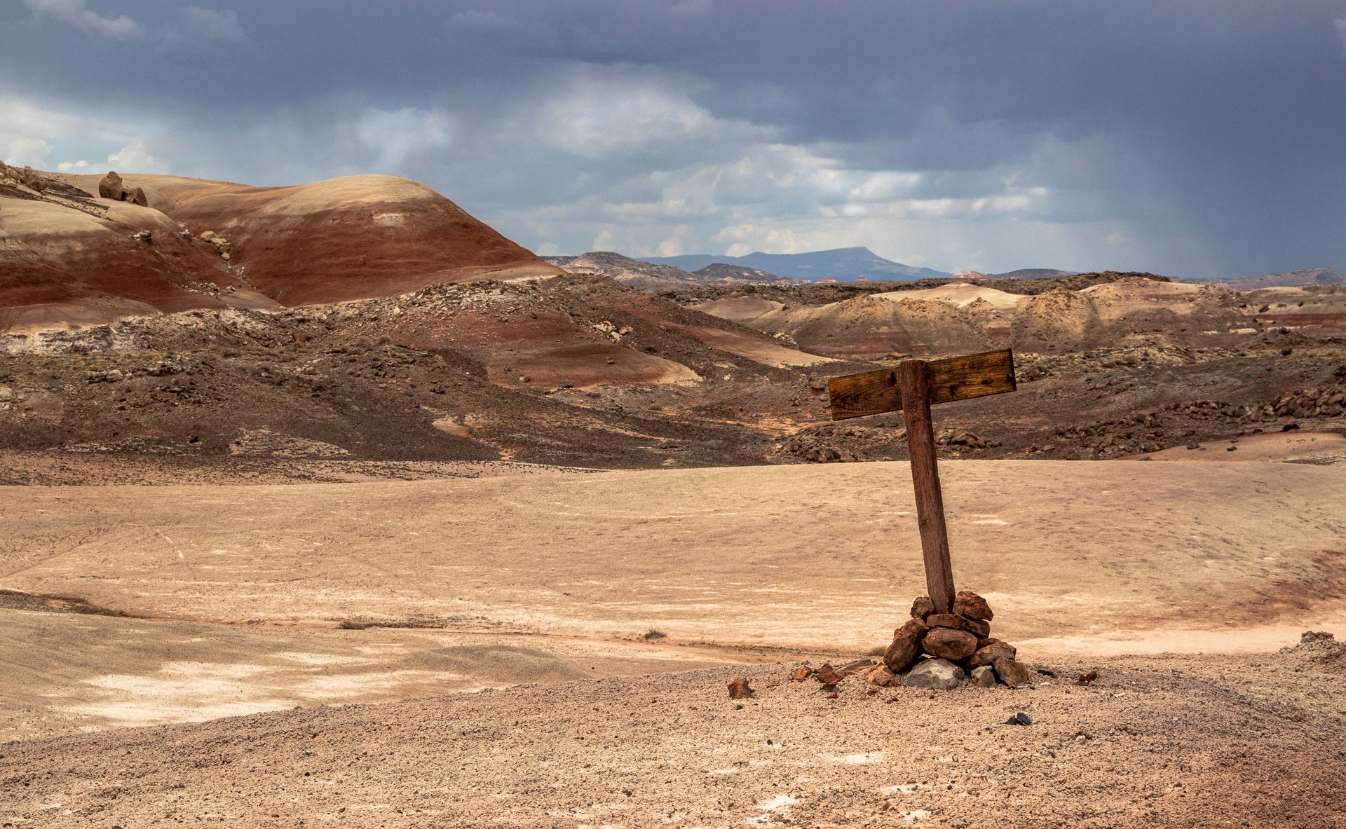 A sign in the middle of a desert with mountains in the background
