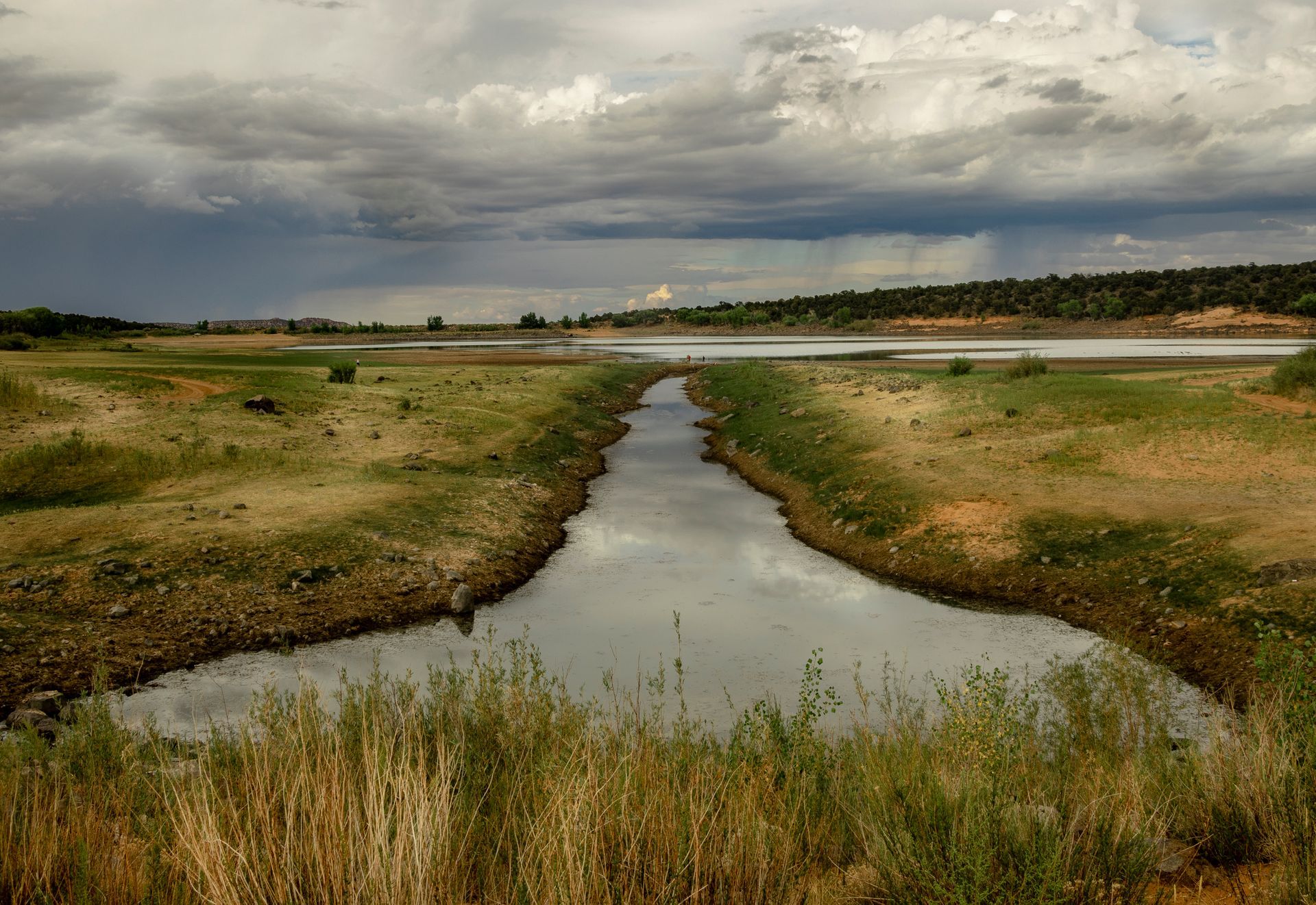 A river running through a grassy field with a cloudy sky in the background.