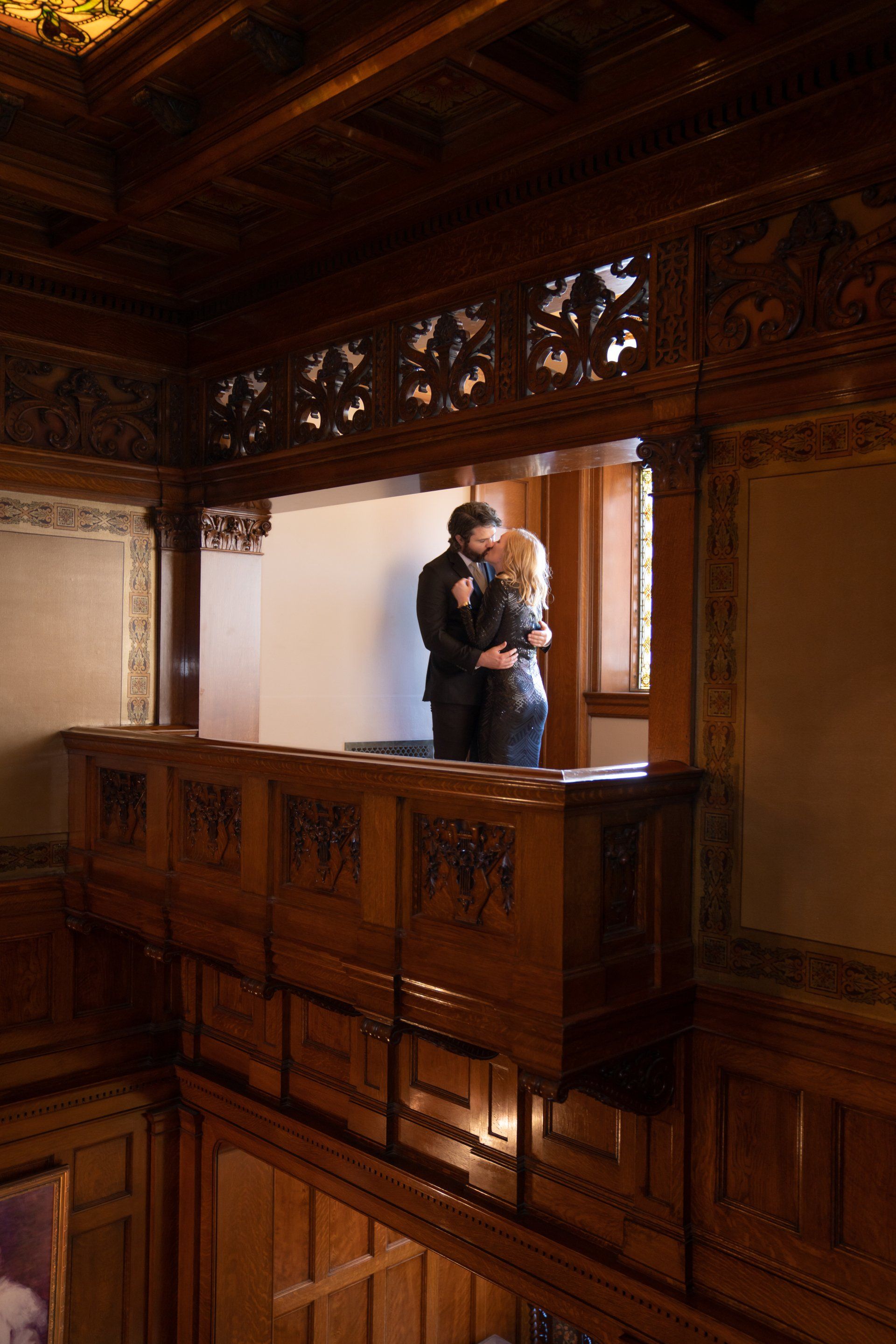 A man and a woman are kissing on a balcony in a room.