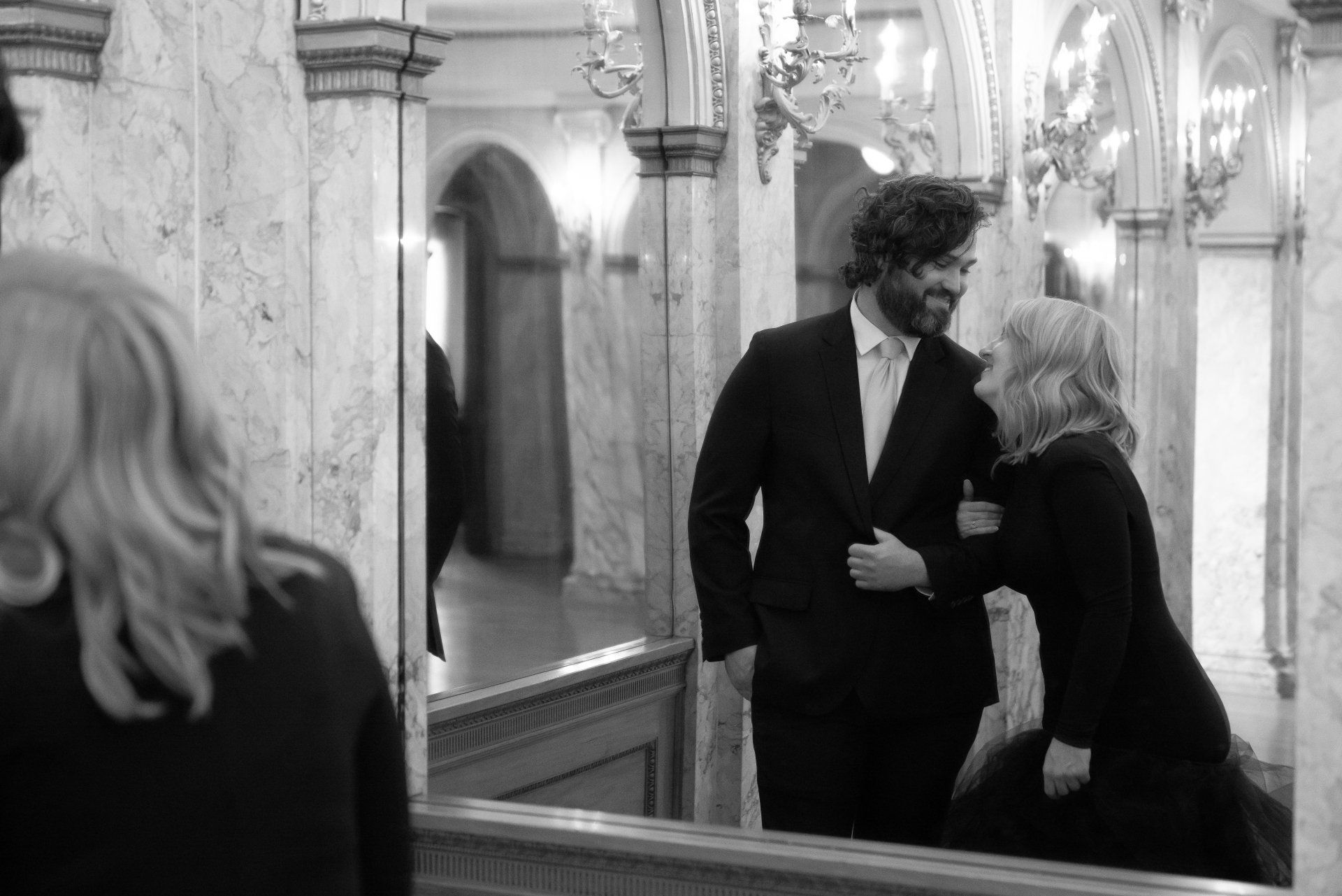 A man and a woman are standing in front of a mirror.