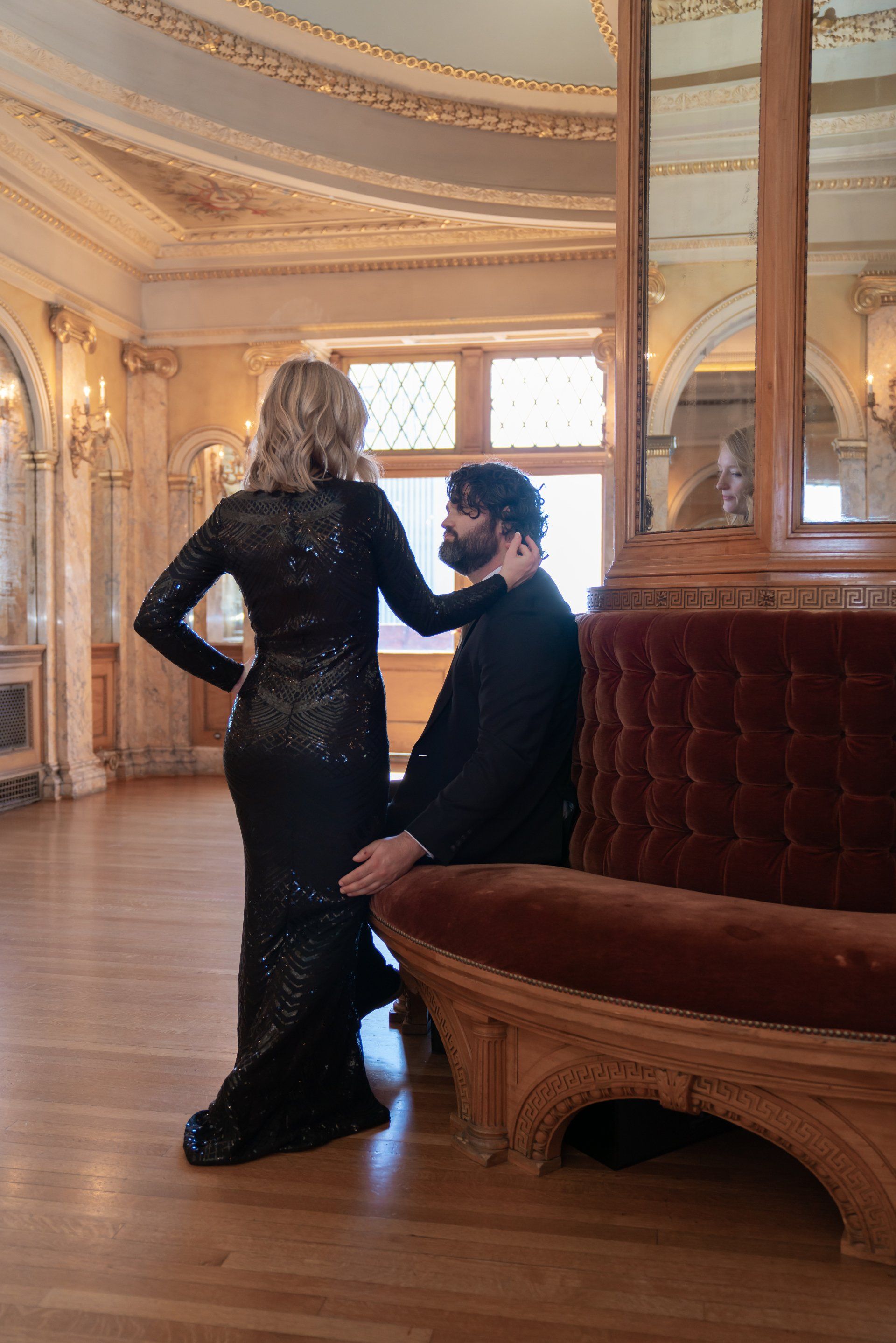 A woman is standing next to a man sitting on a couch in a room.