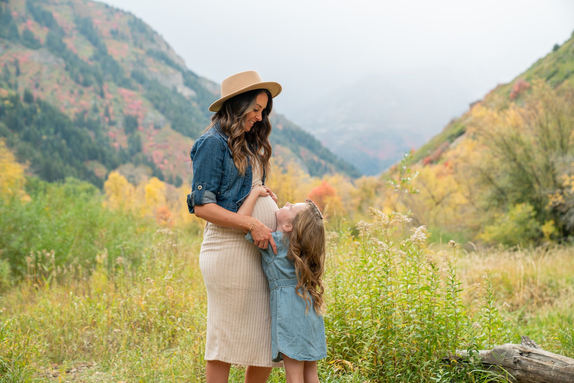 A pregnant woman and a little girl are standing in a field.
