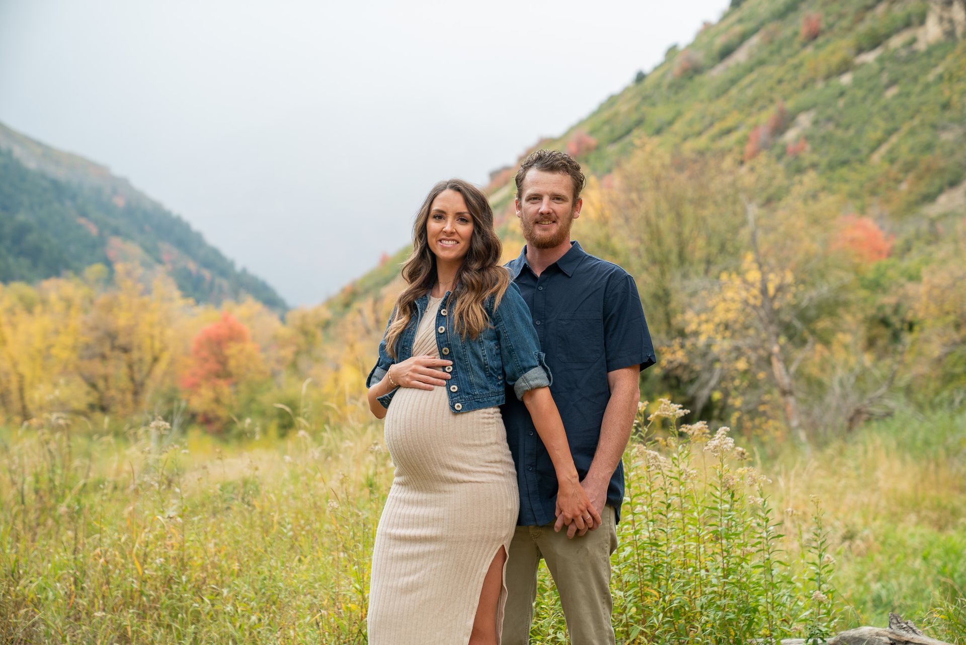 A man and a pregnant woman are standing in a field holding hands.