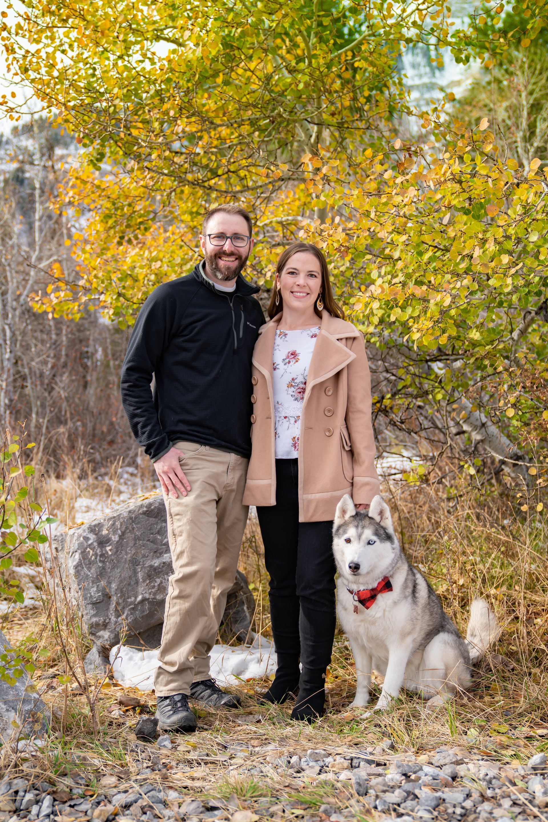 A man and a woman are posing for a picture with their husky dog.