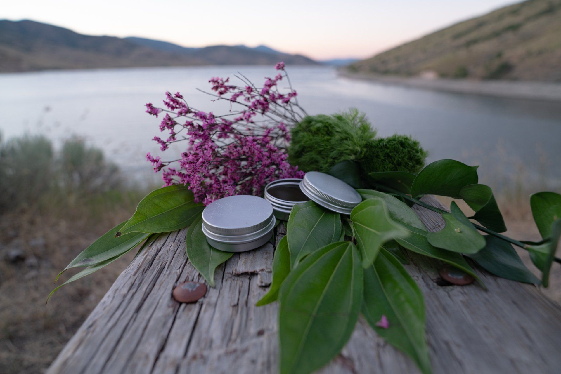 A wooden table with flowers and leaves on it in front of a lake.