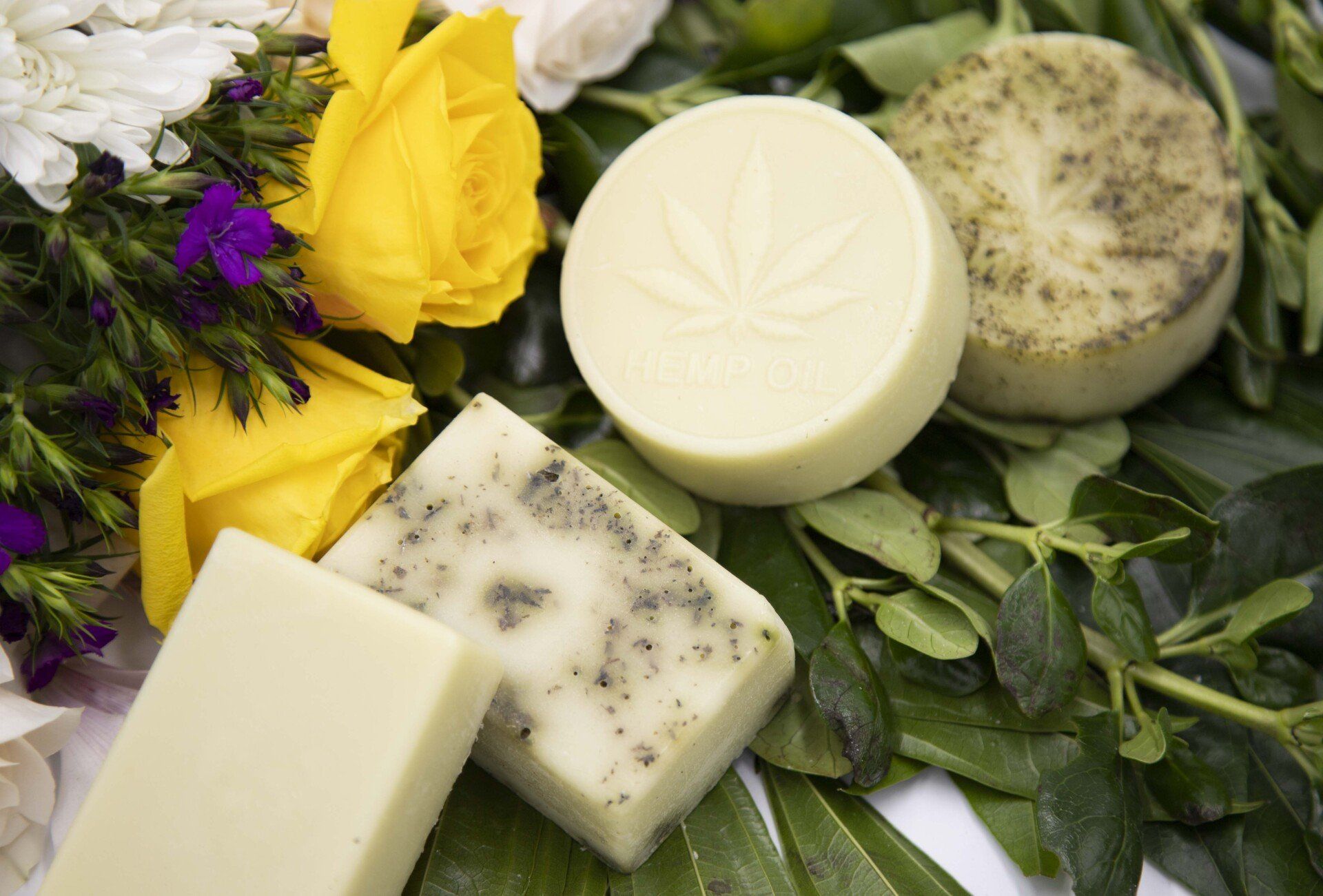 Three bars of soap are sitting on a table next to flowers and leaves.