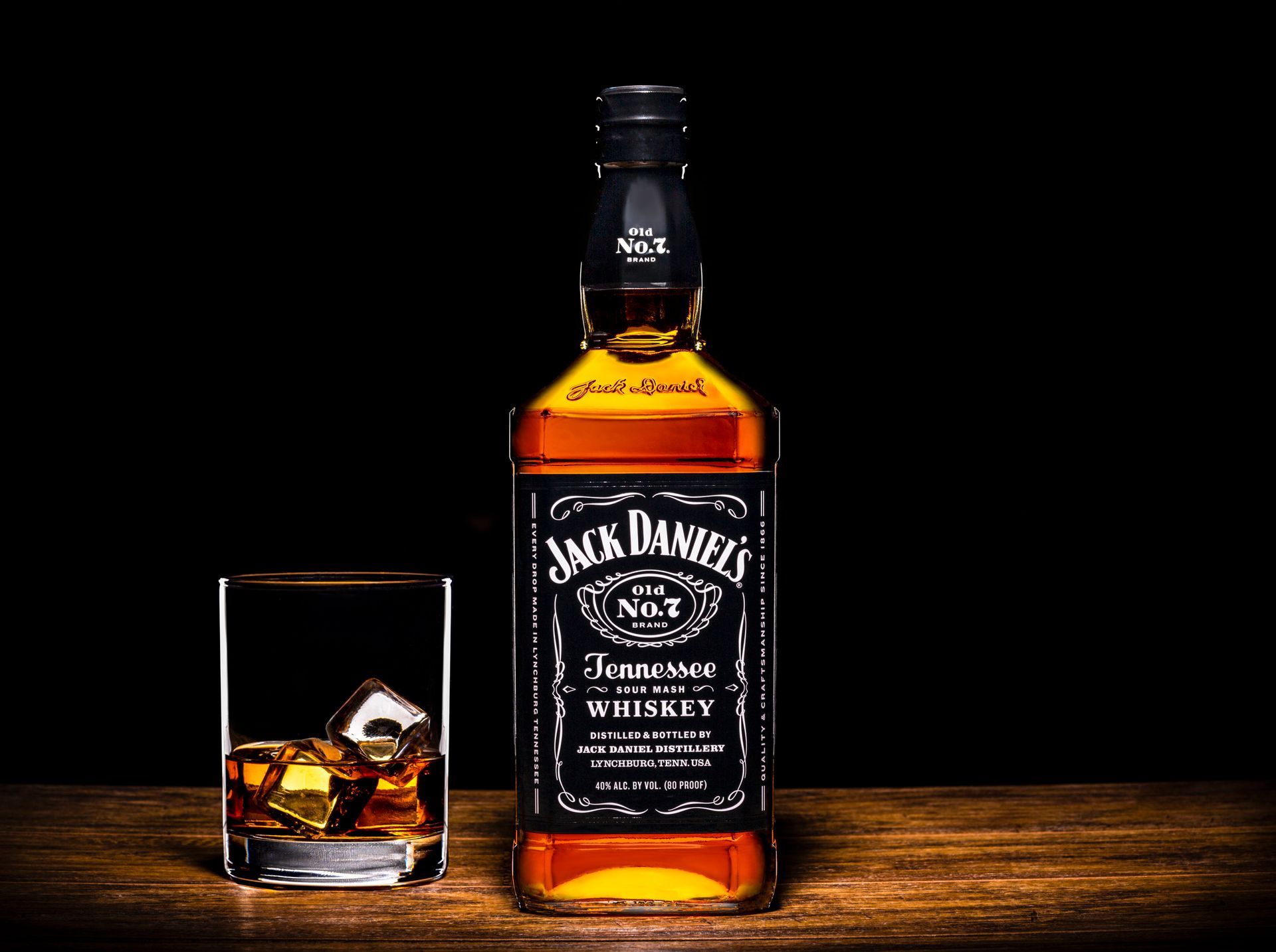 A bottle of jack daniel 's whiskey and a glass of whiskey on a wooden table.