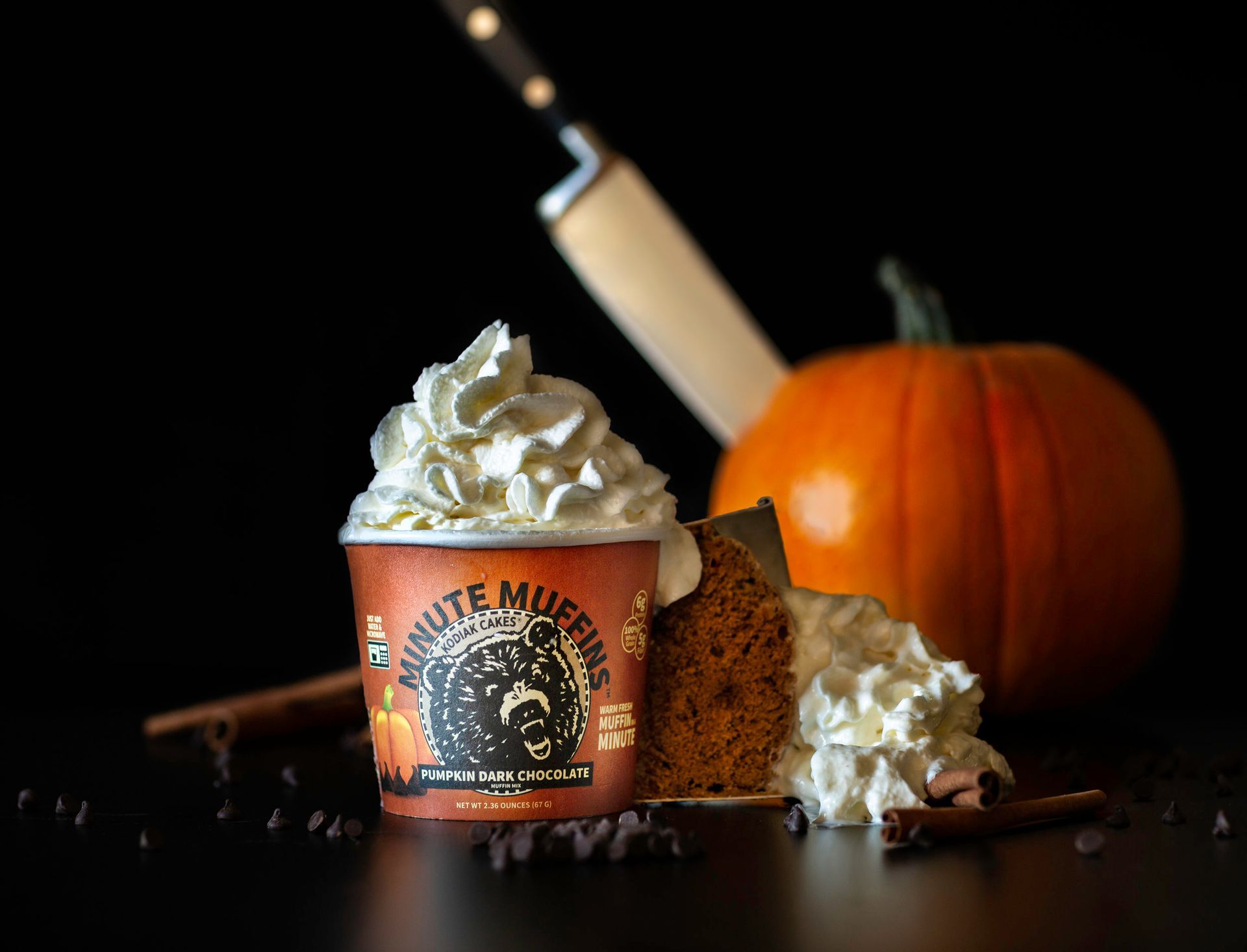 A cup of pumpkin muffins with whipped cream and a pumpkin in the background