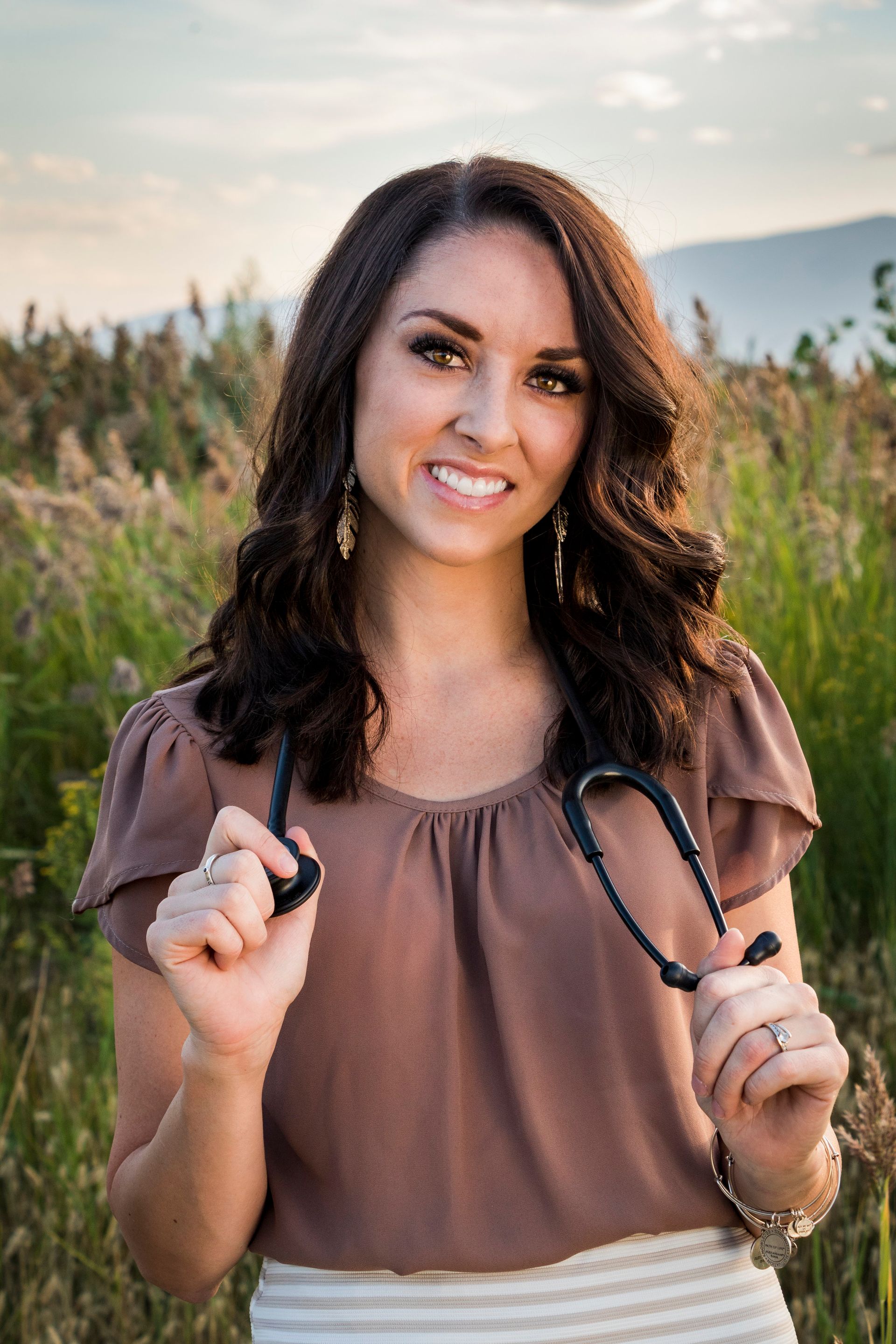 A woman is holding a stethoscope in a field and smiling.